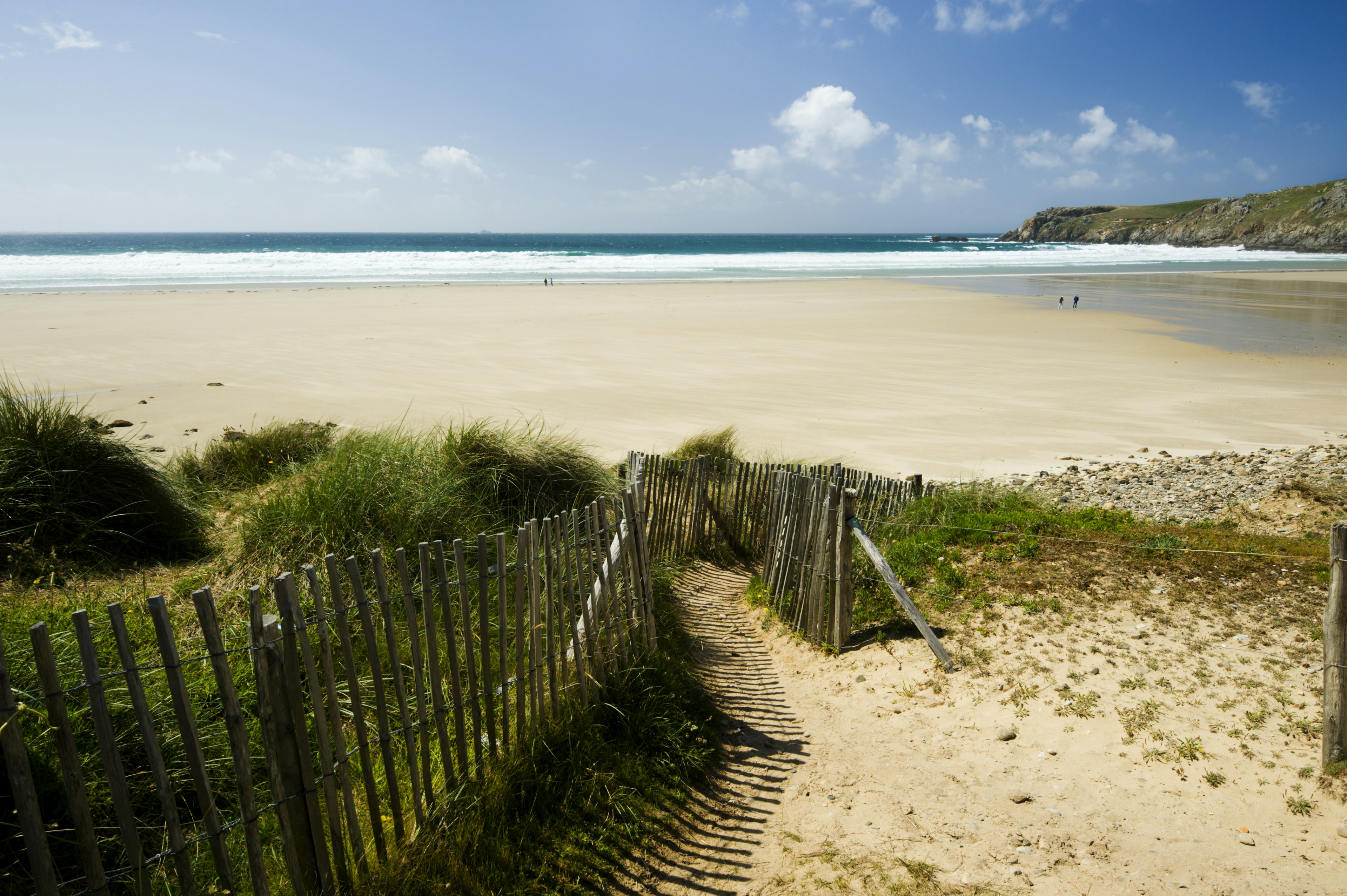 A white sandy beach with a couple of people walking on it on the north coast of France.