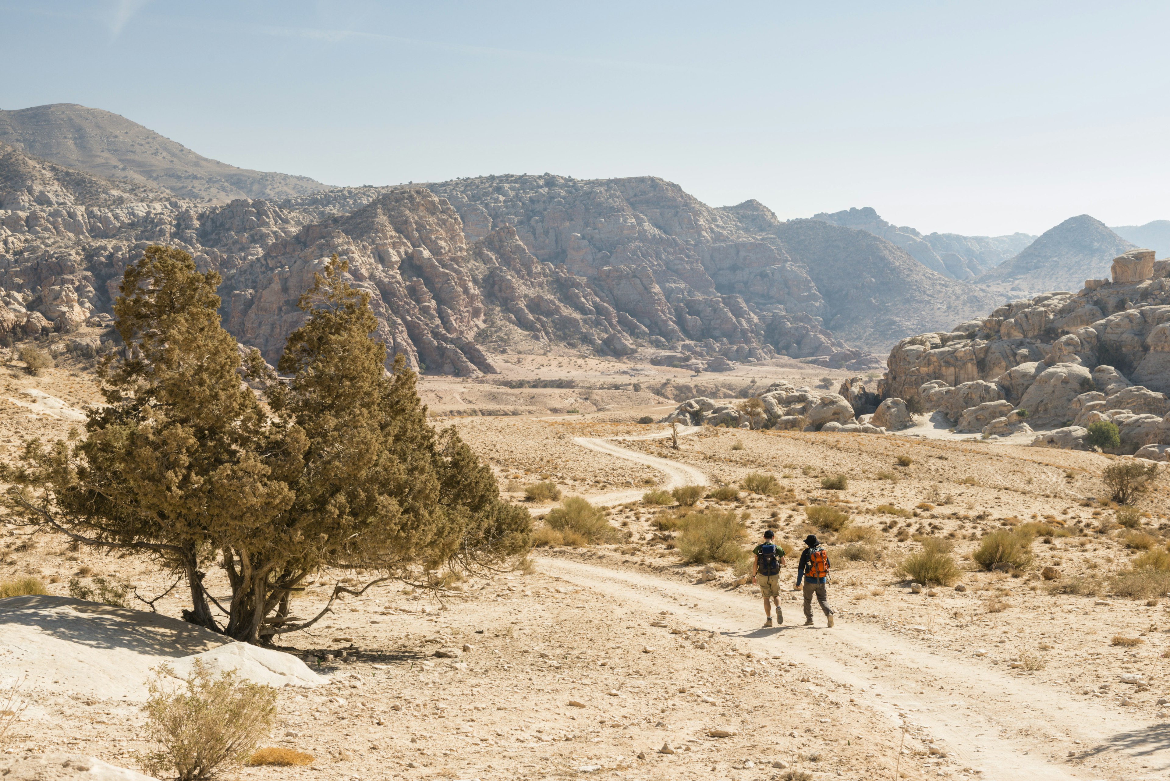 Two hikers follow a dirt trail across a desert landscape