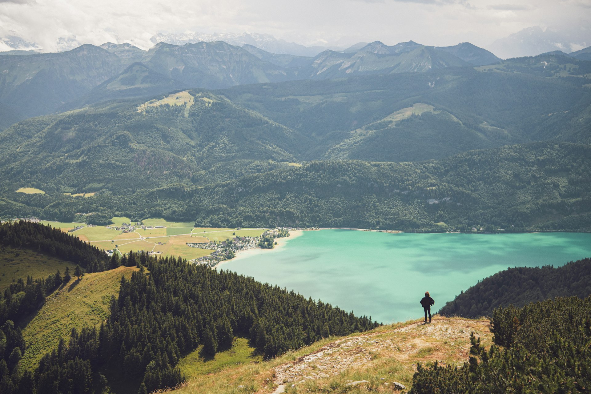 Man standing on Schafberg Mountain, Austria, overlooking a lake.