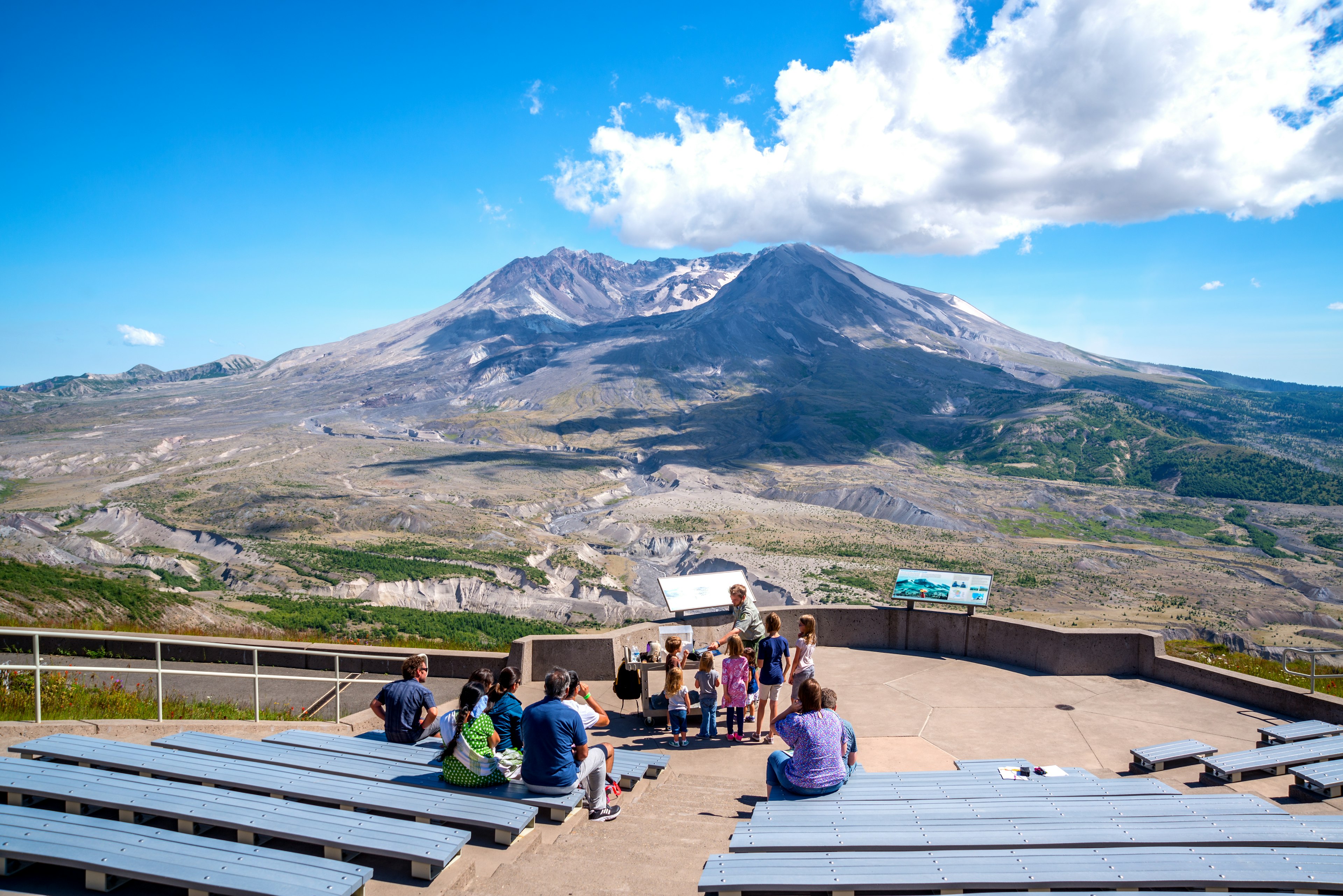 A park ranger gives a talk to tourists in front of a volcanic landscape