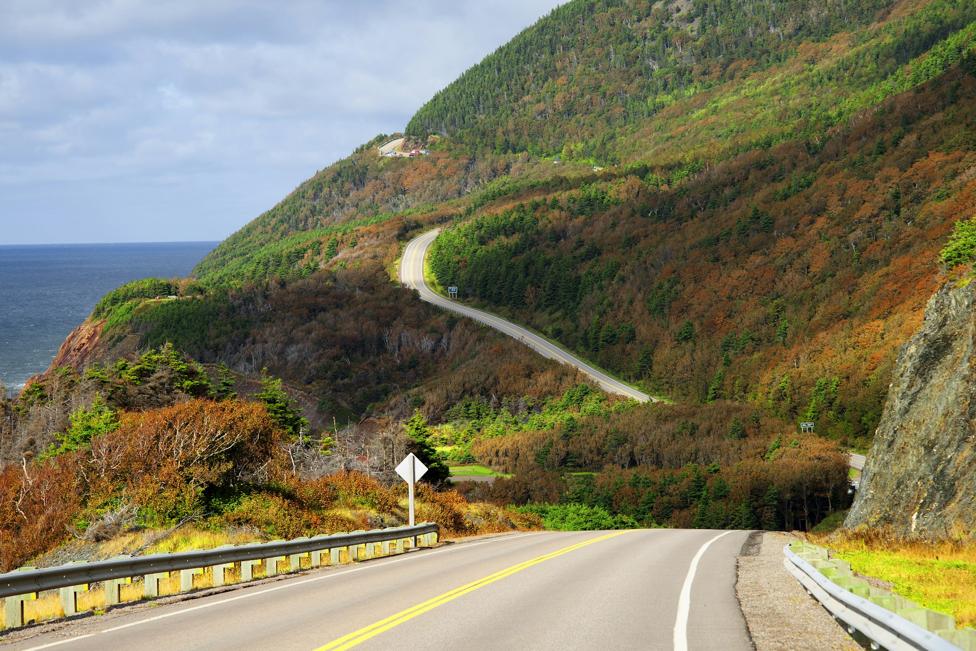 Uma estrada se desenrola com o mar de um lado e a dramática folhagem de outono do outro, Cabot Trail, Cape Breton, Nova Escócia, Canadá