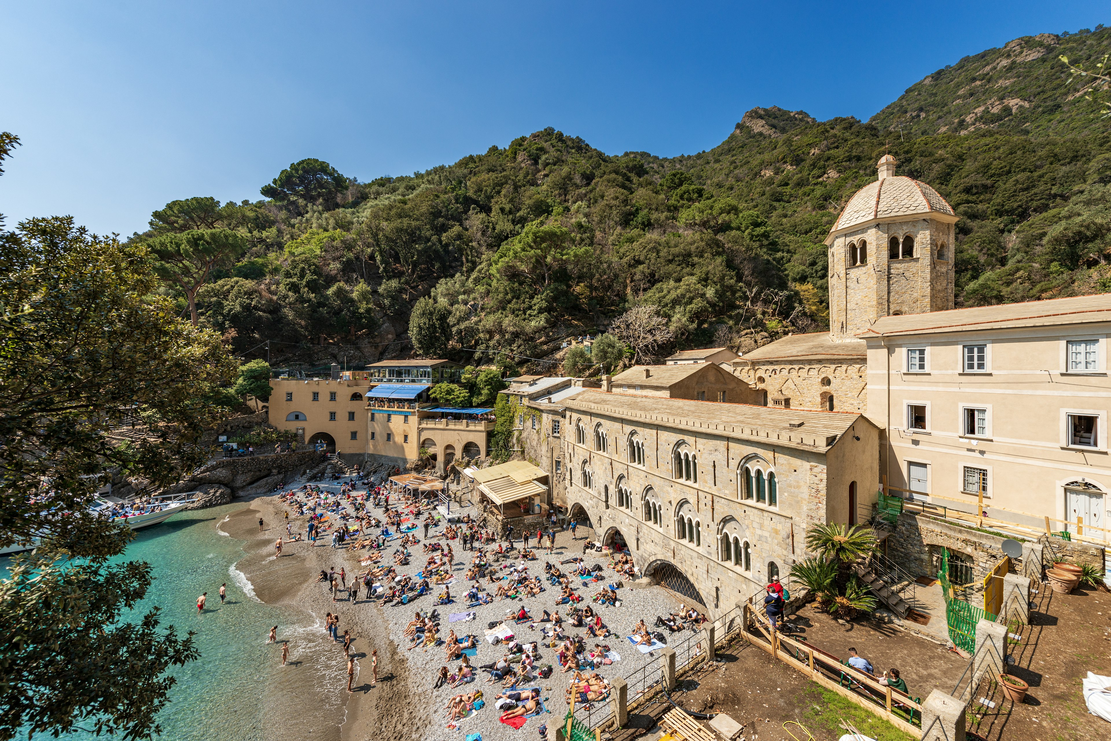 A large number of tourists sunbathe and relax on the small beach on a sunny spring day in Genoa, Italy