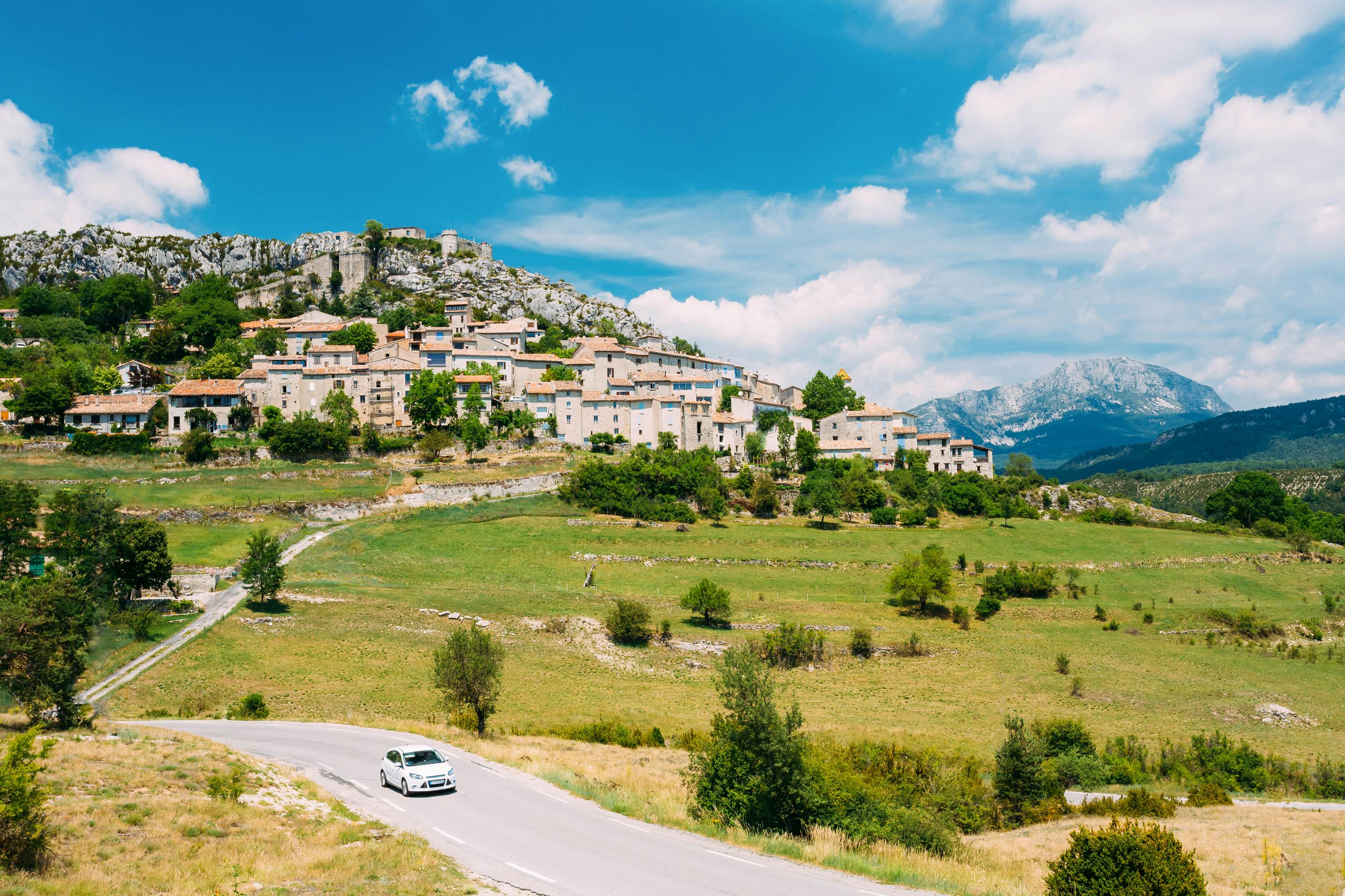 A car drives along the road against a background of beautiful scenic view of a medieval village in France.