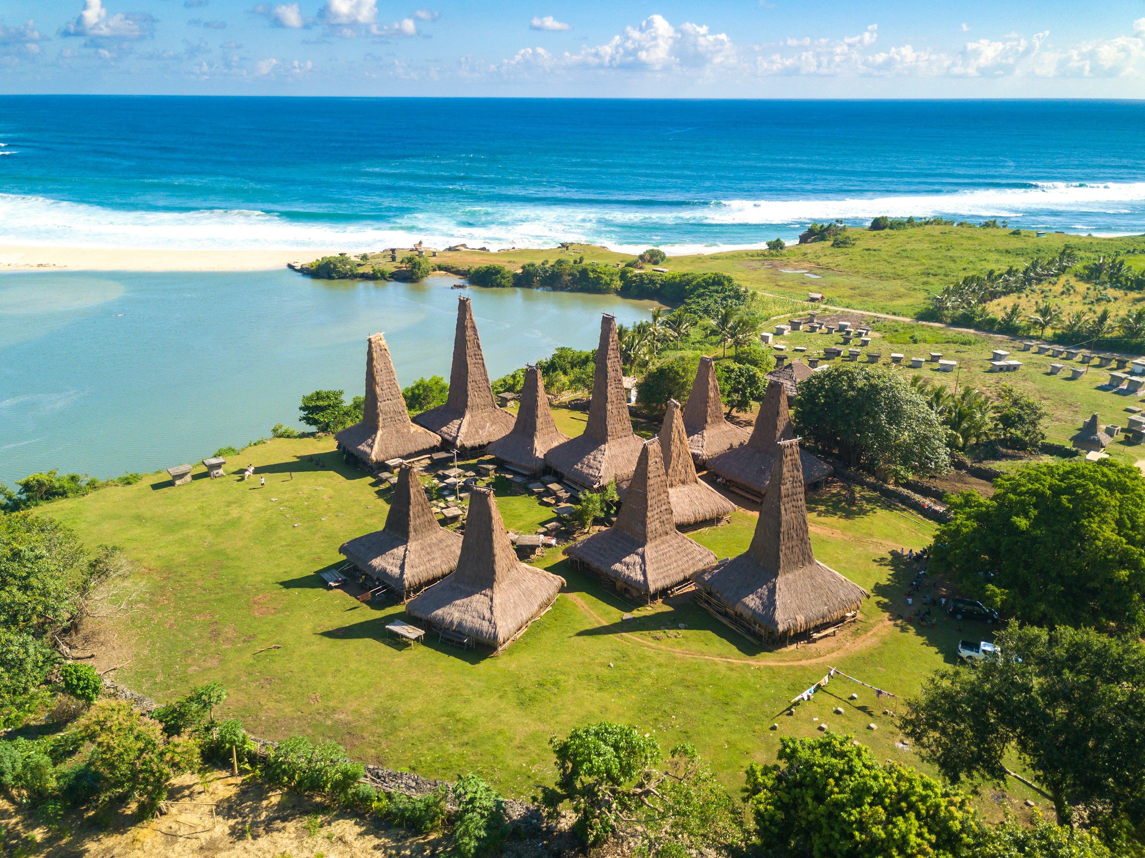 A series of thatched structures with a tall central spire on the edge of a tropical beach