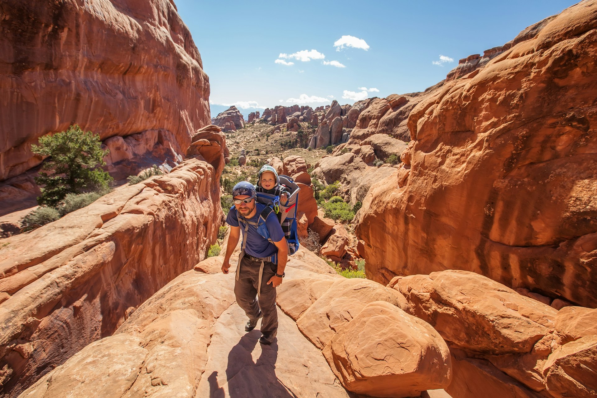 Man carrying a baby in a backpack hiking and enjoying the thrills of Arches National Park