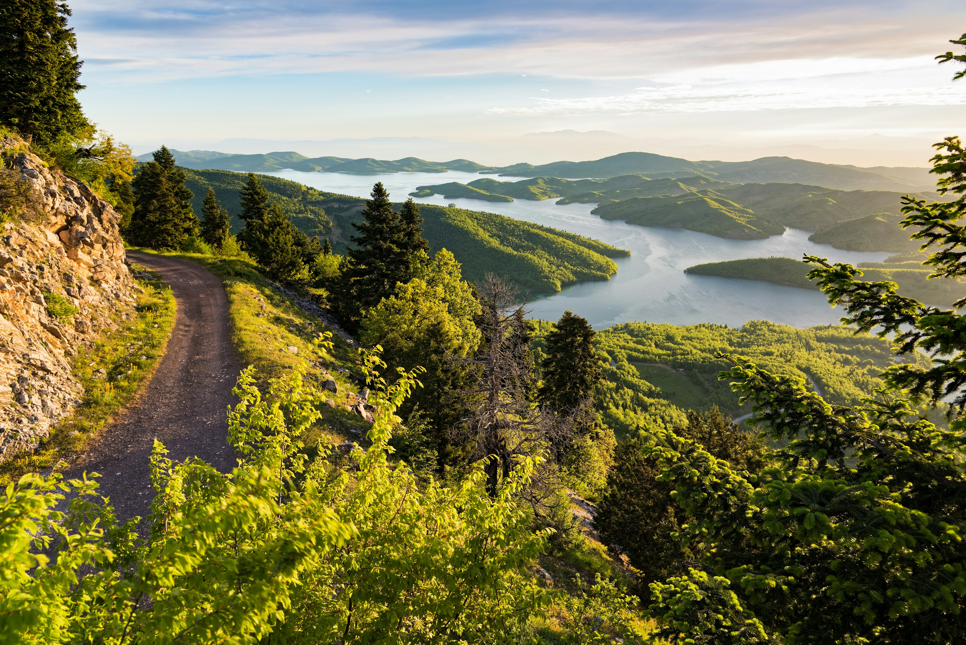 The sun rises over a lush green forest with an artificial lake in Greece.