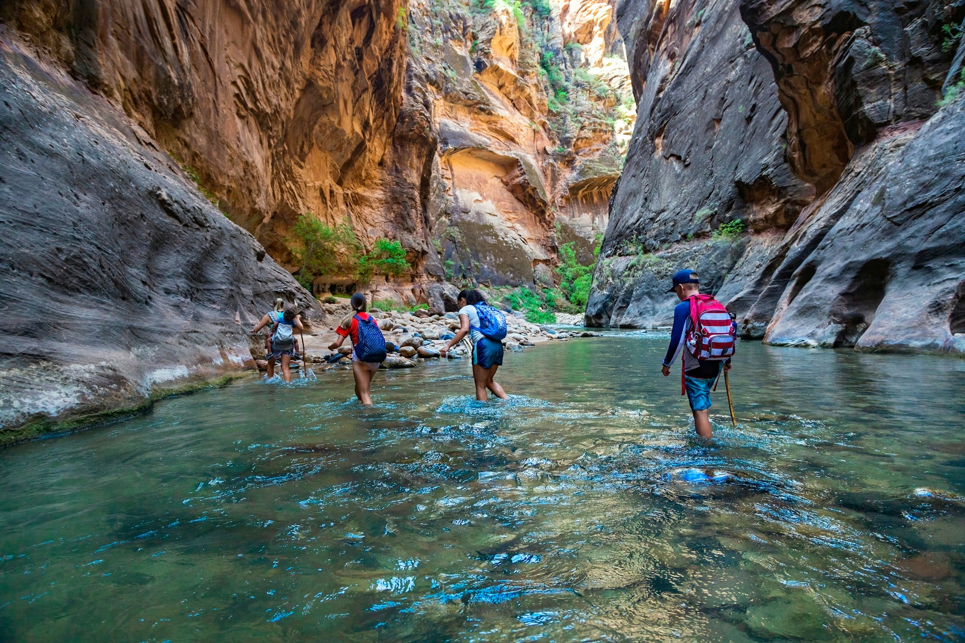 Hikers wade through a river in a narrow slot canyon
