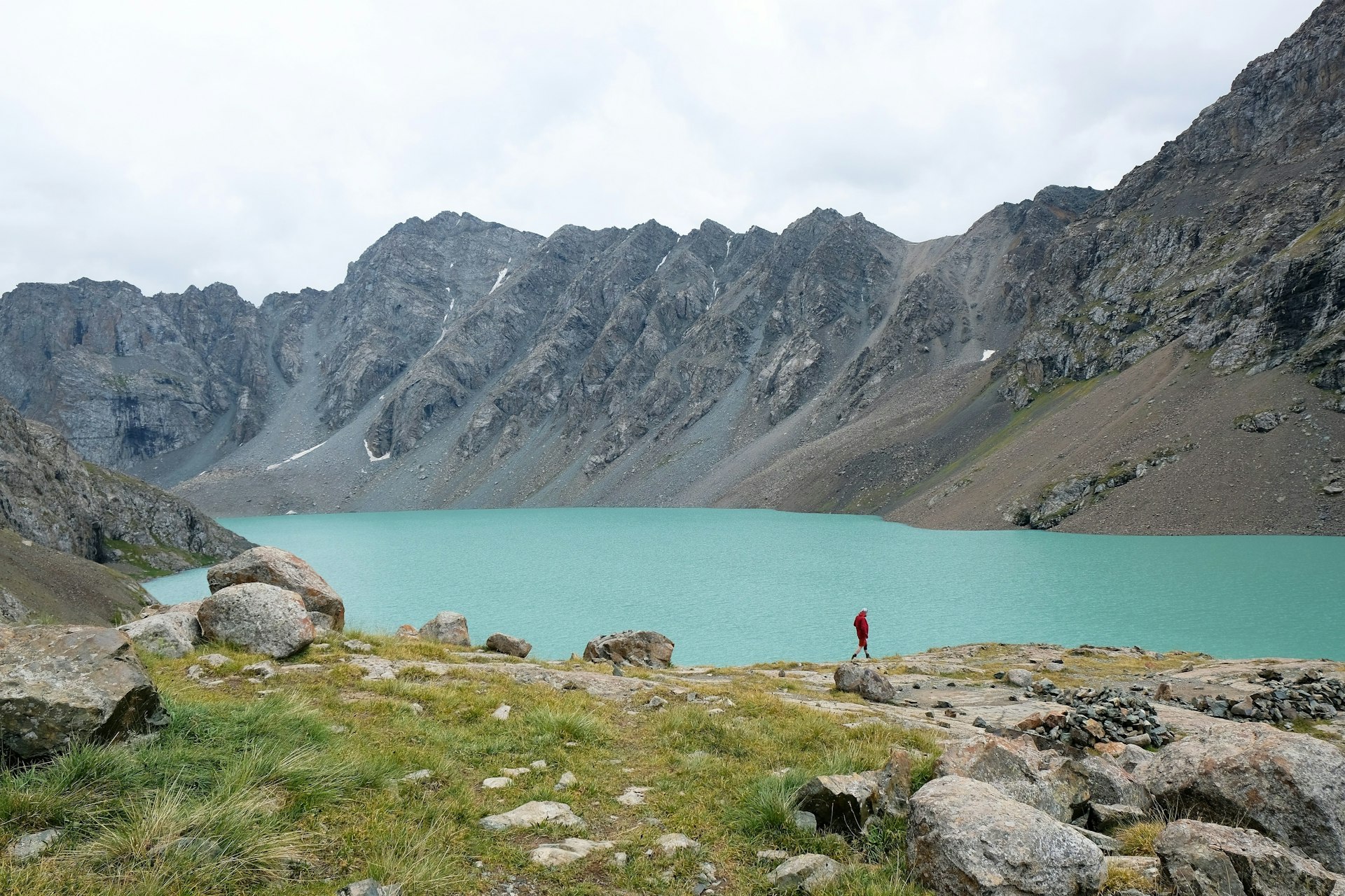 A sole hiker walking near the edge of a turquoise alpine lake