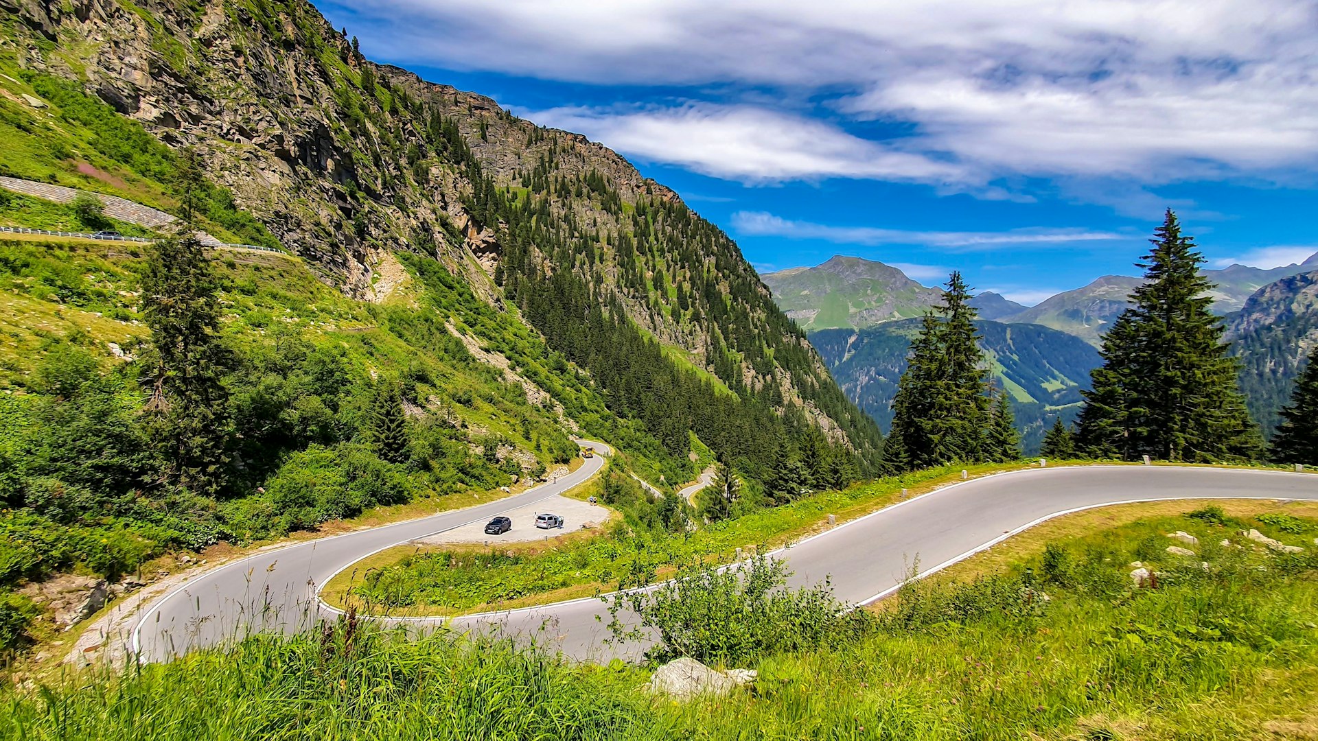 Cars on a road with tight bends winding through a mountainous region in the sunshine