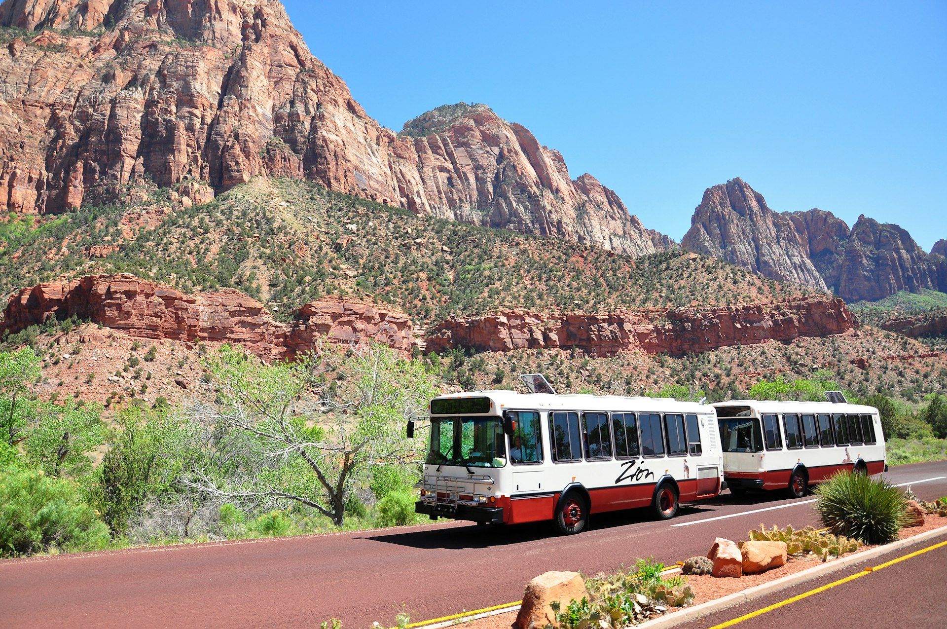 A bus with two separate compartments drive on a road through a red-rock canyon