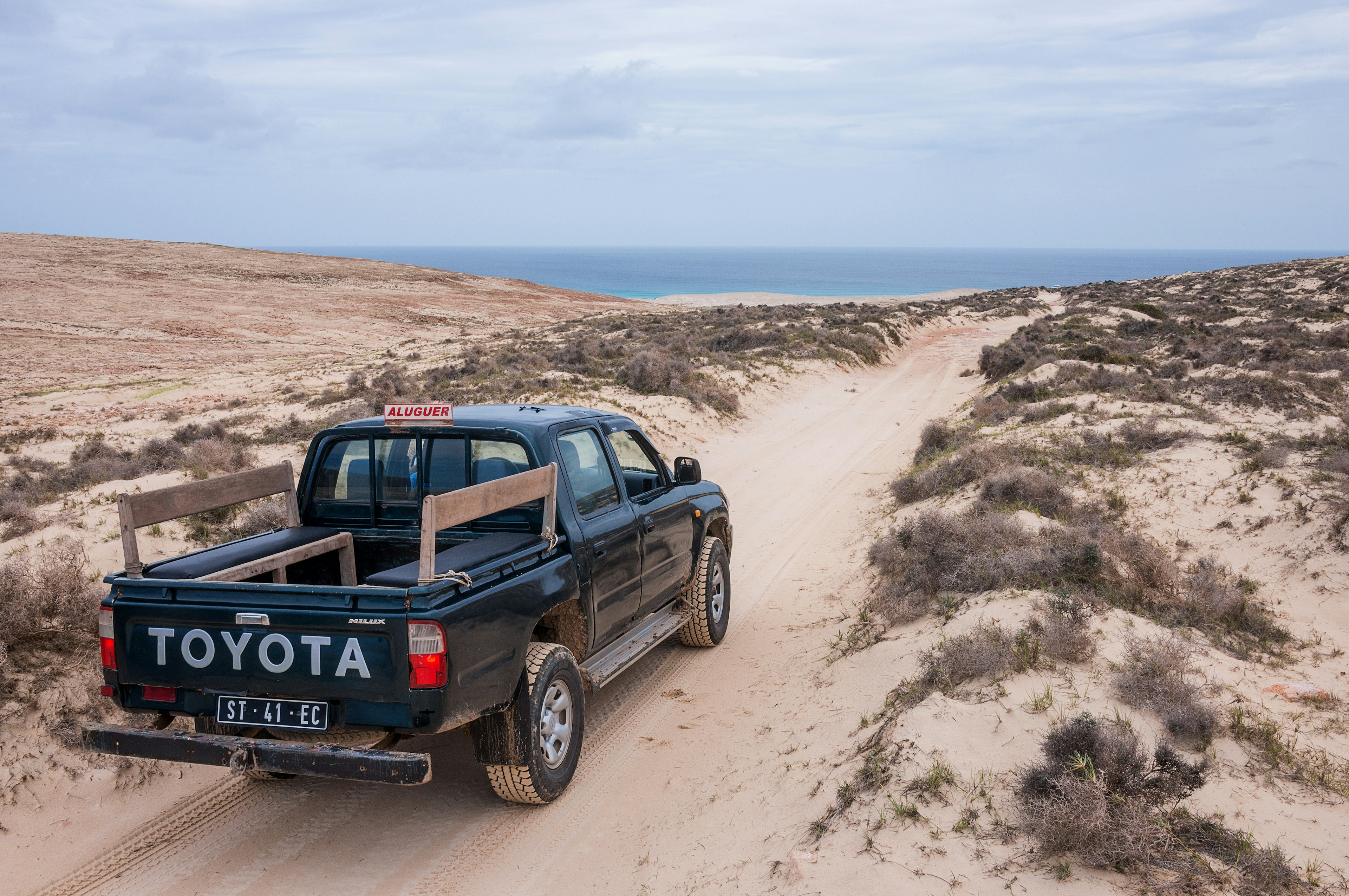 A four-wheel drive vehicle makes its way down a sandy track heading towards the ocean