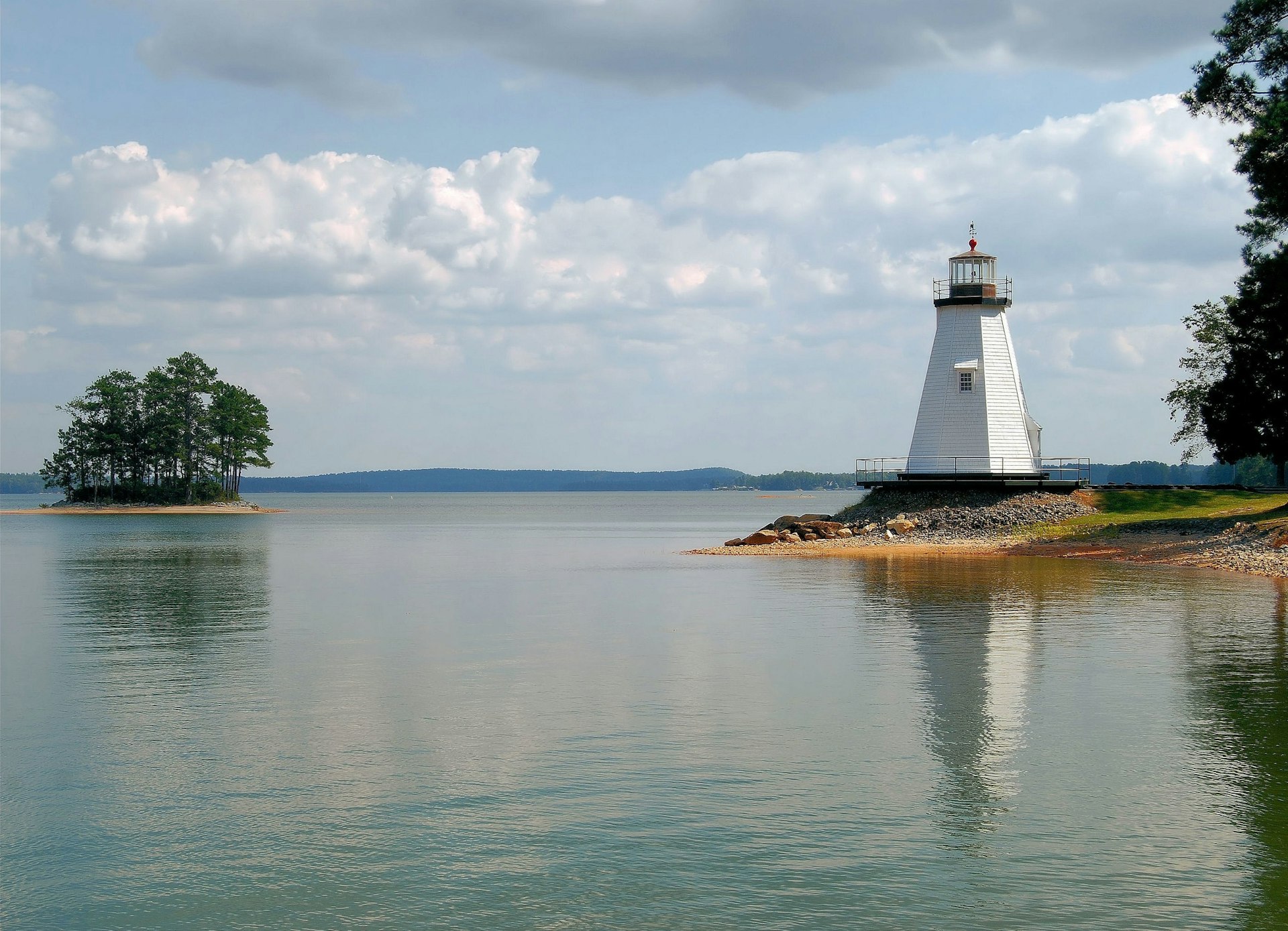 A small lighthouse sits on the side of a lush lake. 
