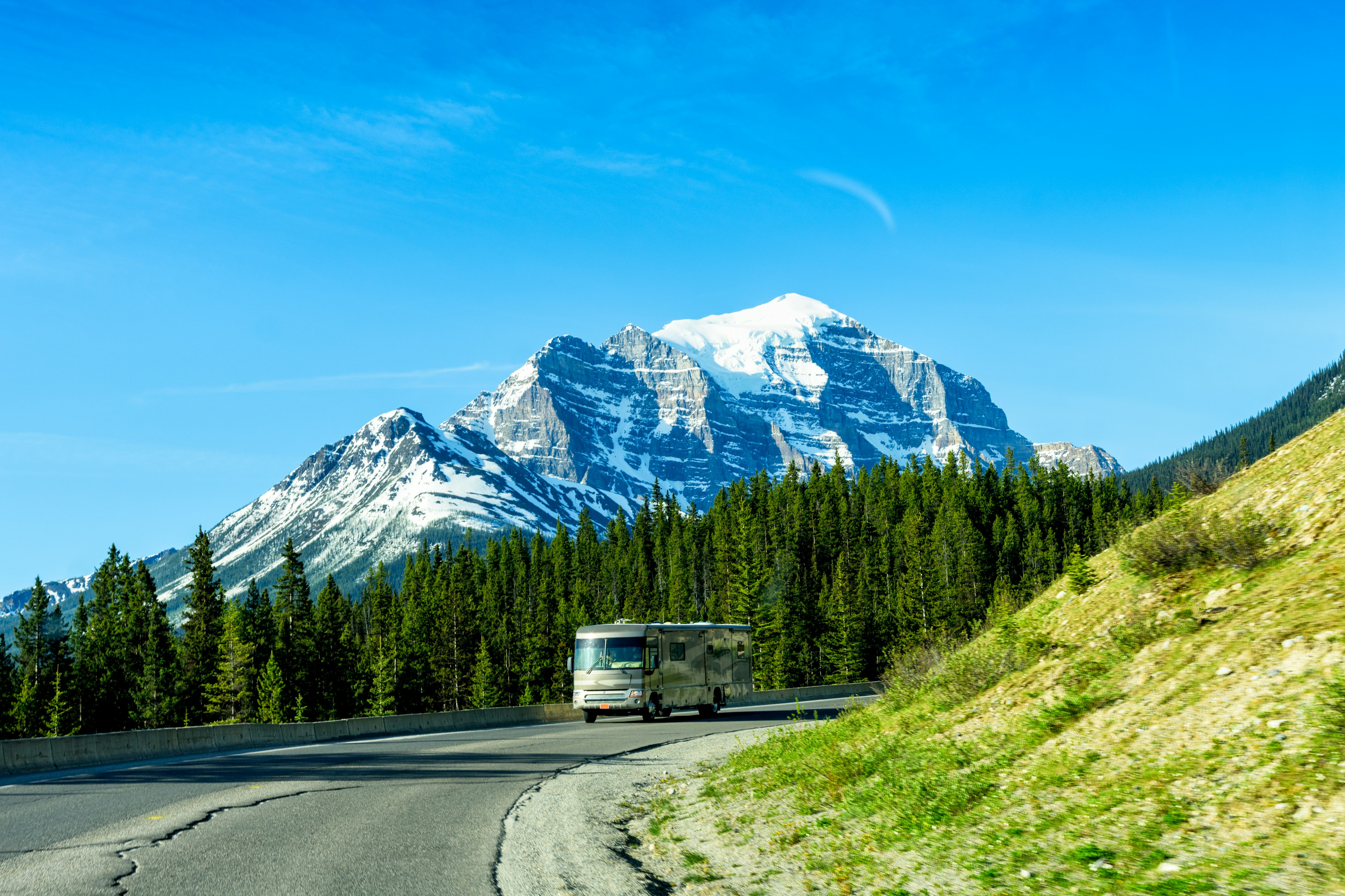 A large motorhome drives around a bend on a road through a forested mountain landscape