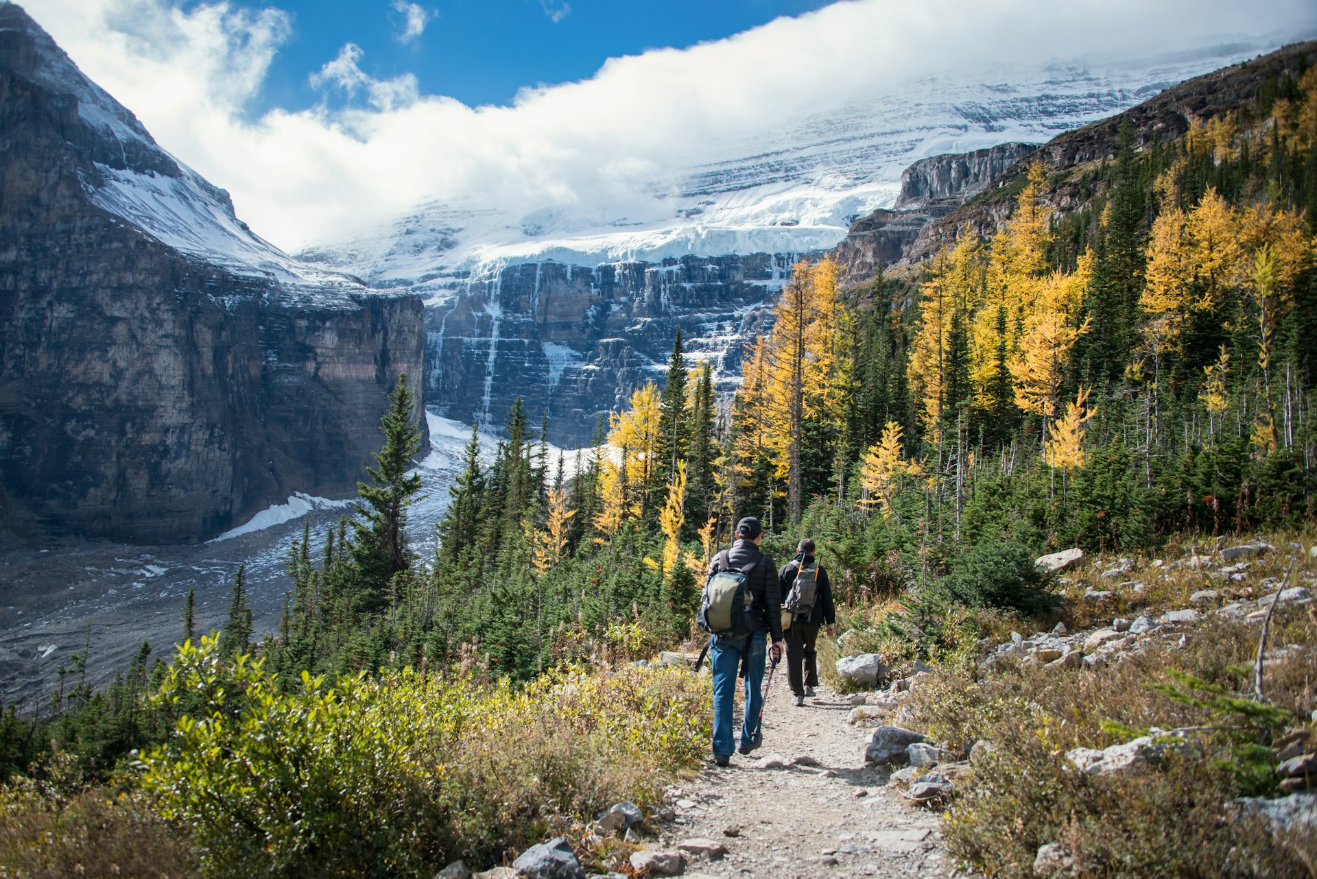 Two hikers walk down a path in front of the high mountains of Banff National Park. 