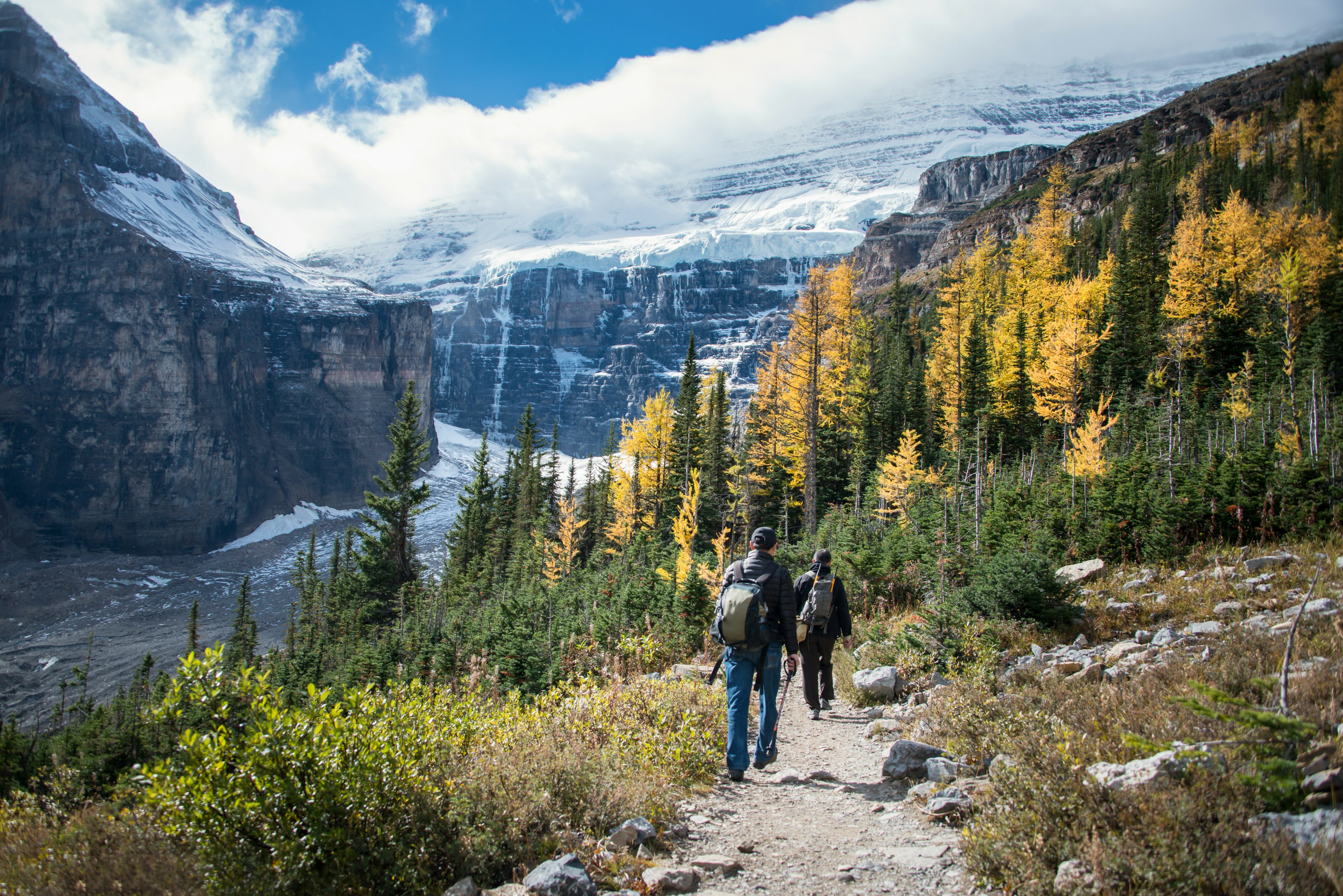 Two hikers walk down a path in front of the high mountains of Banff National Park.