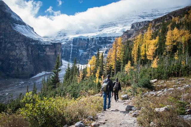 Two hikers walk down a path in front of the high mountains of Banff National Park.