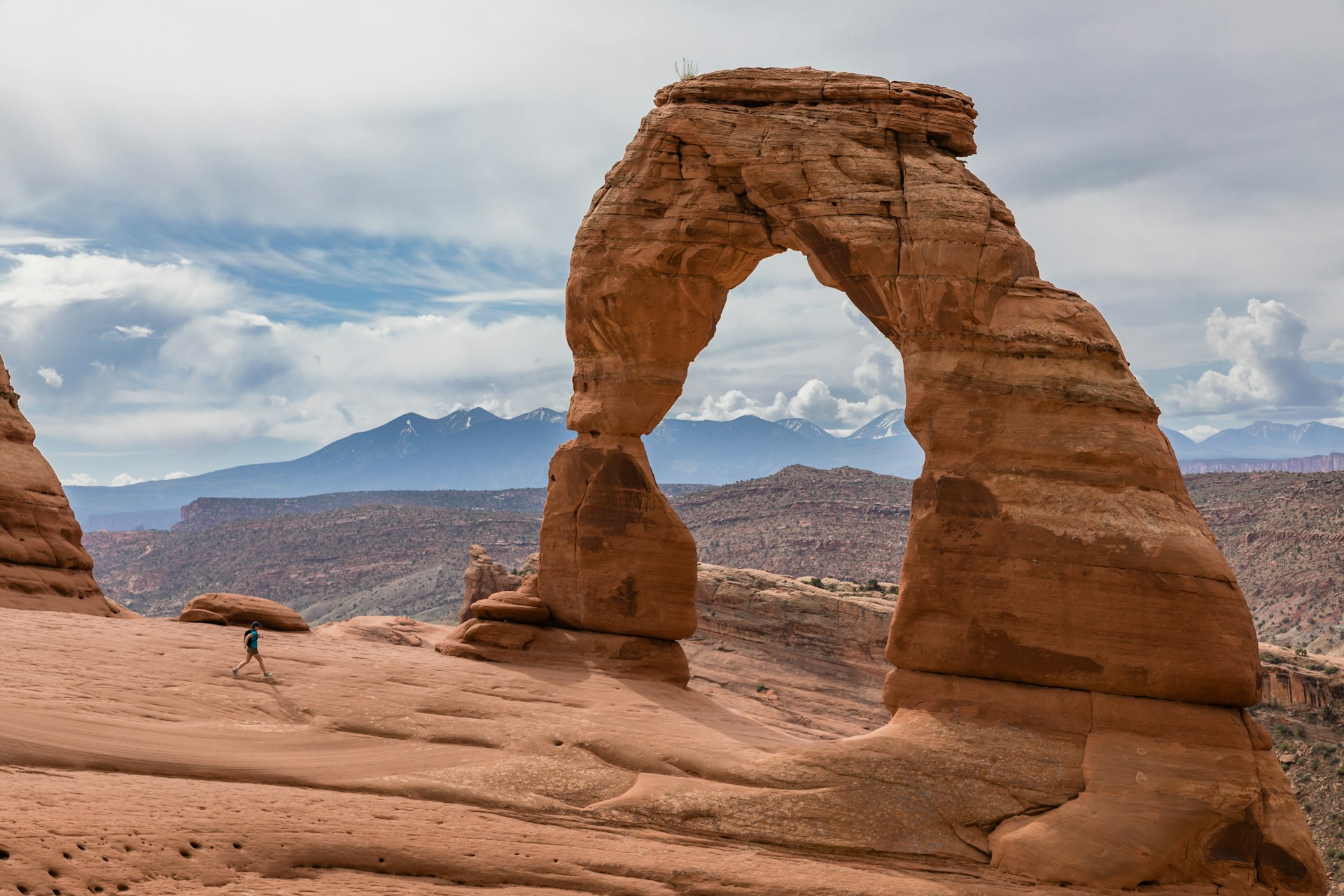 A person looks tiny in comparison to a vast archway of rock that towers above them