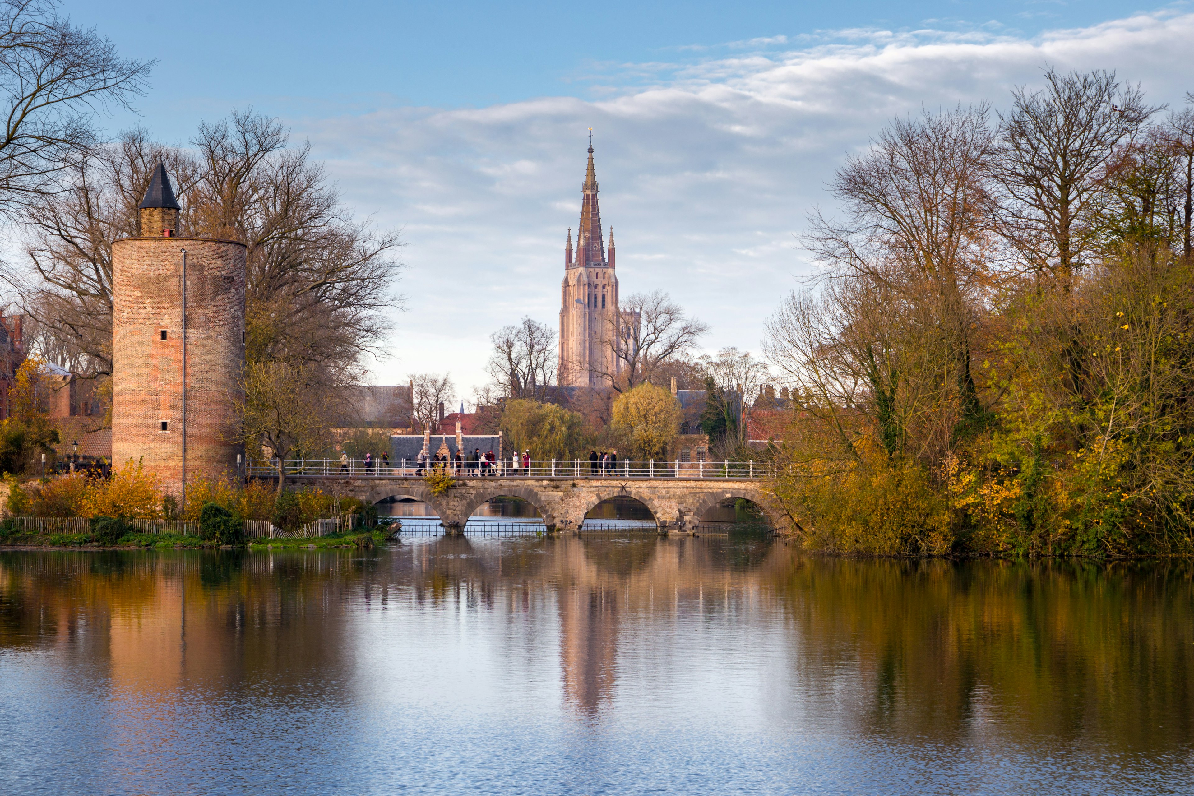 A few people cross a bridge in front of a church