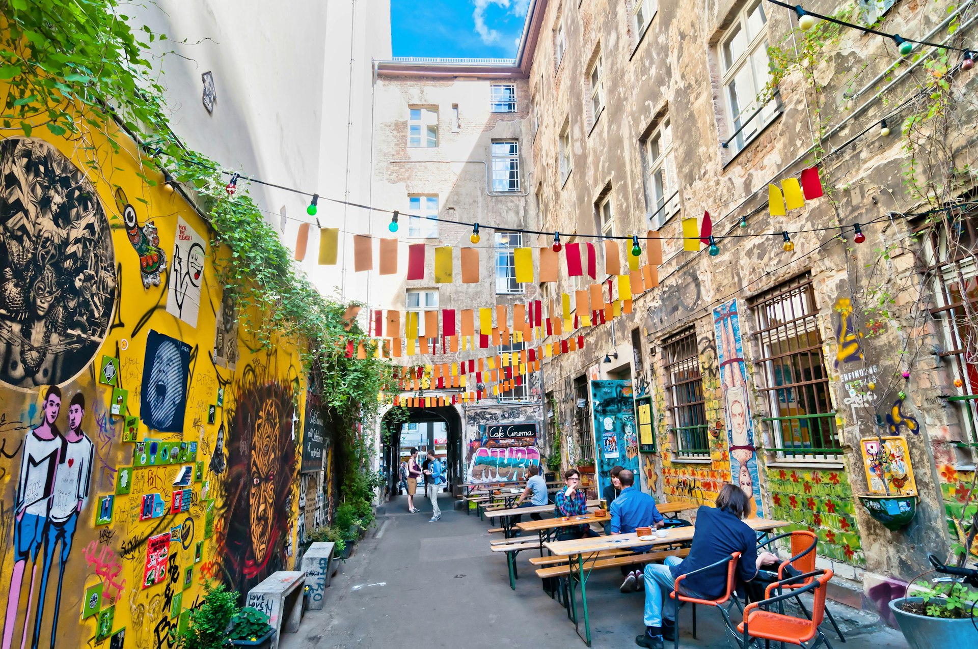 People seated at a small laneway with graffiti and colorful street art lining the walls