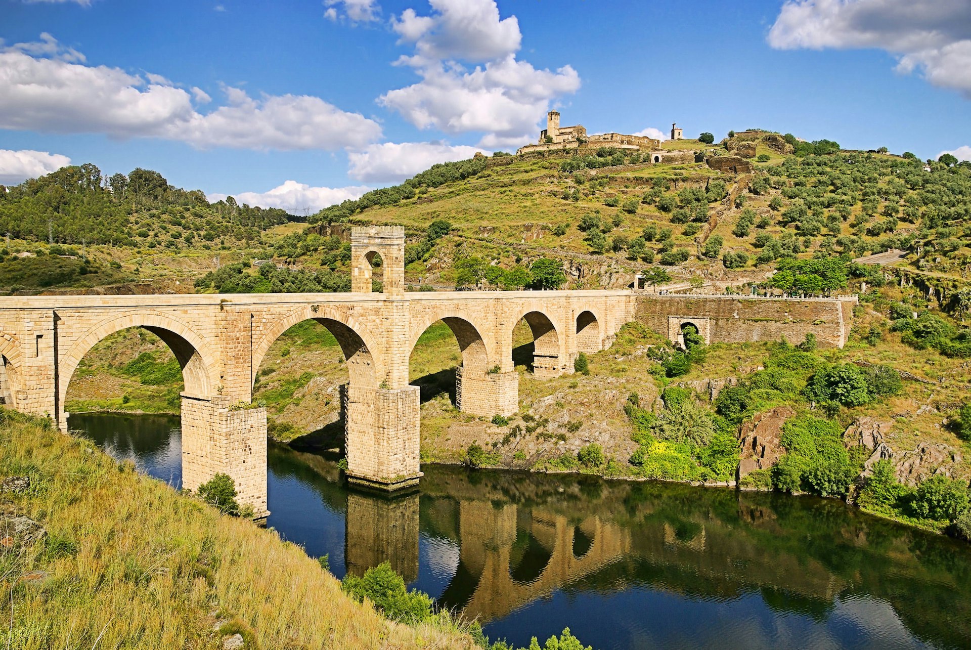 A historic bridge arches over a river in Extramadura, Spain. 