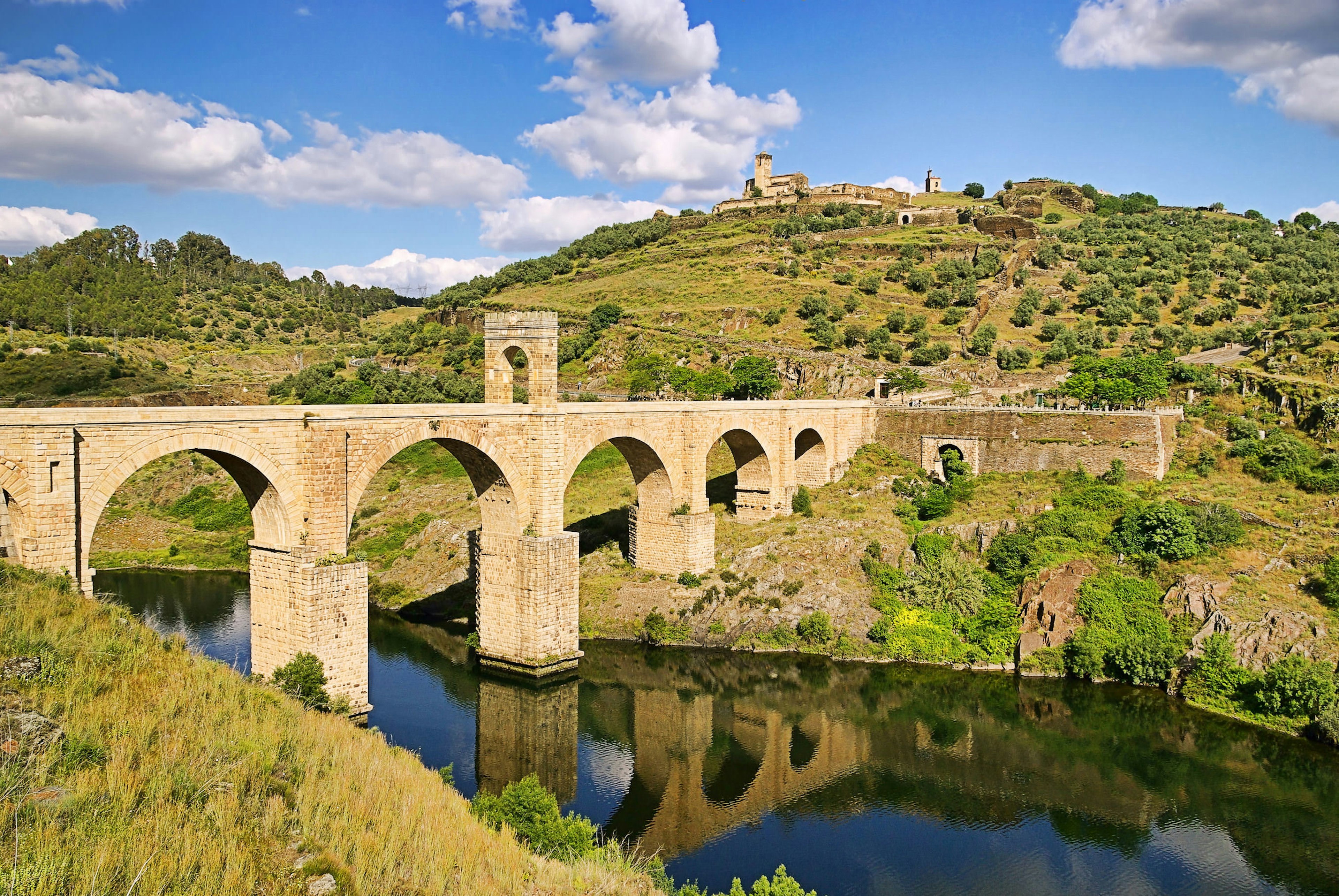 A historic bridge arches over a river in Extramadura, Spain.