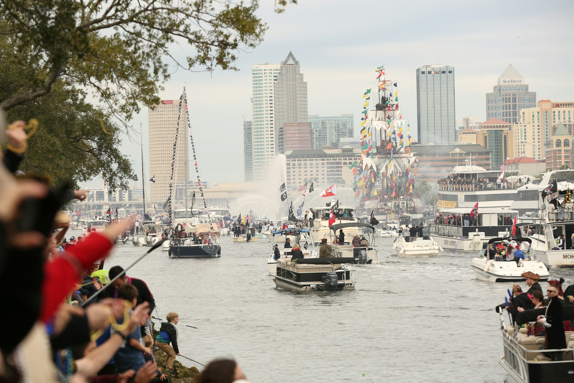 People watch from shore as boats sail into Tampa Bay as part of the pirate-themed festival Gasparilla