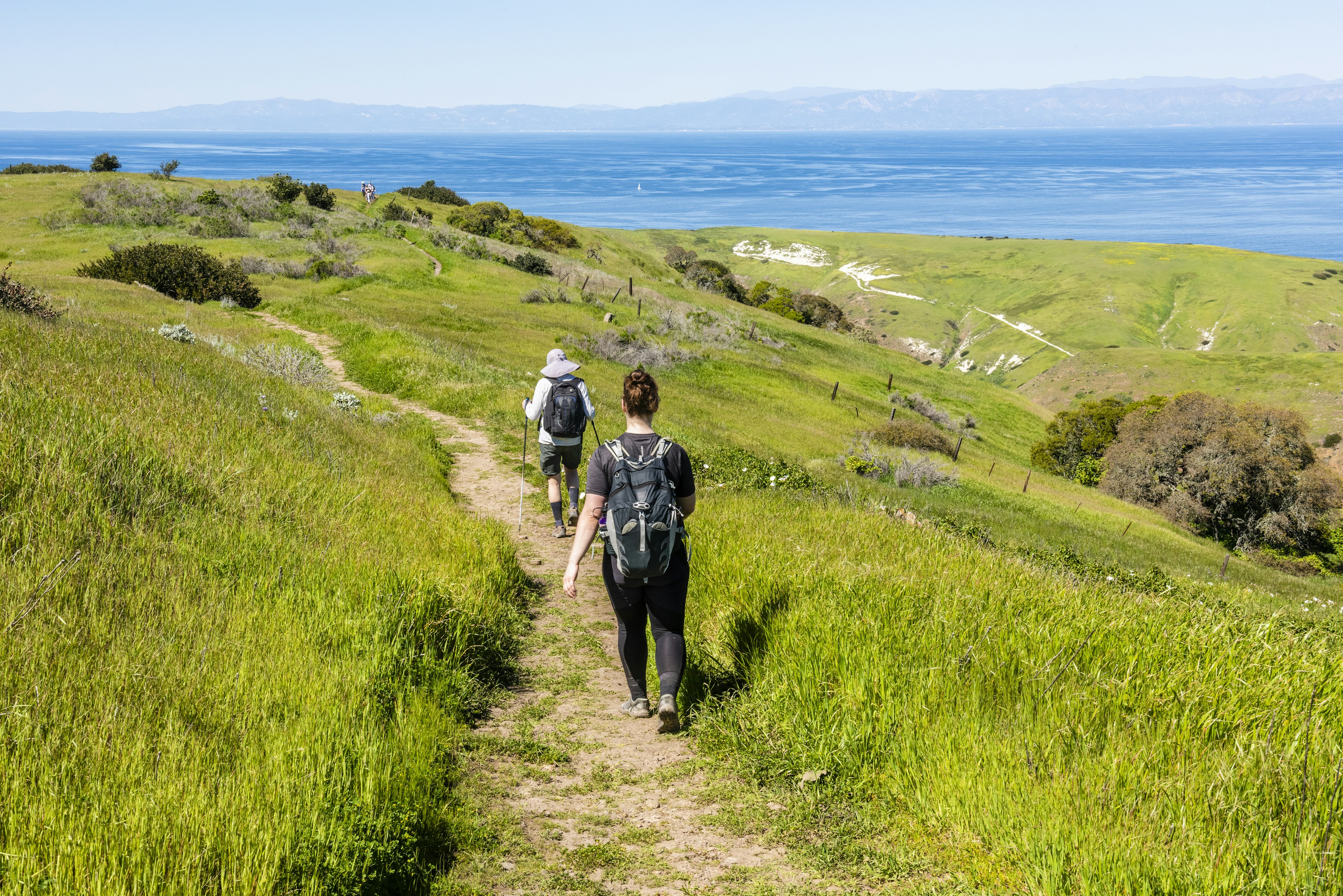 Two people following a hiking trail downhill towards the sea