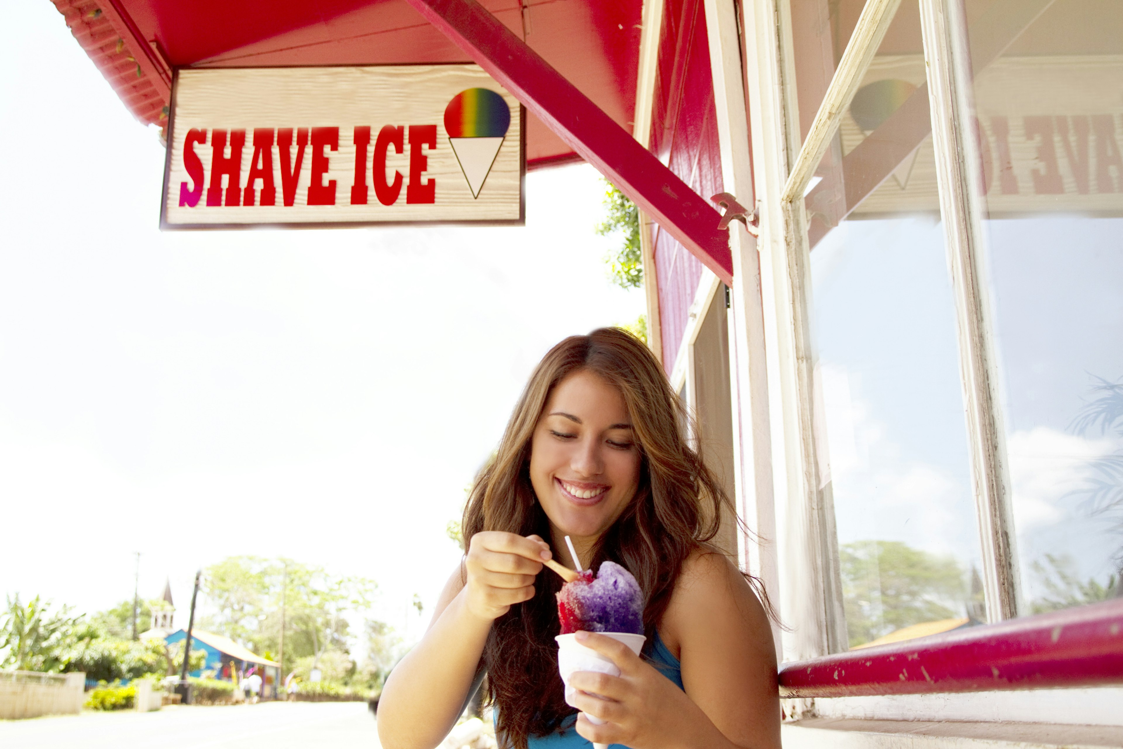 Woman smiles and eats shave ice outside a store in Hawaii