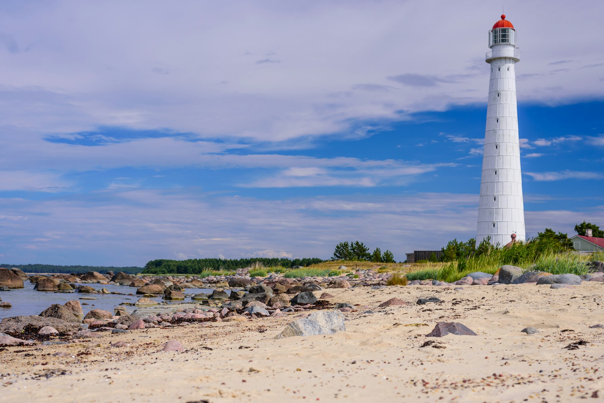 A large white lighthouse on a deserted rocky and sand beach