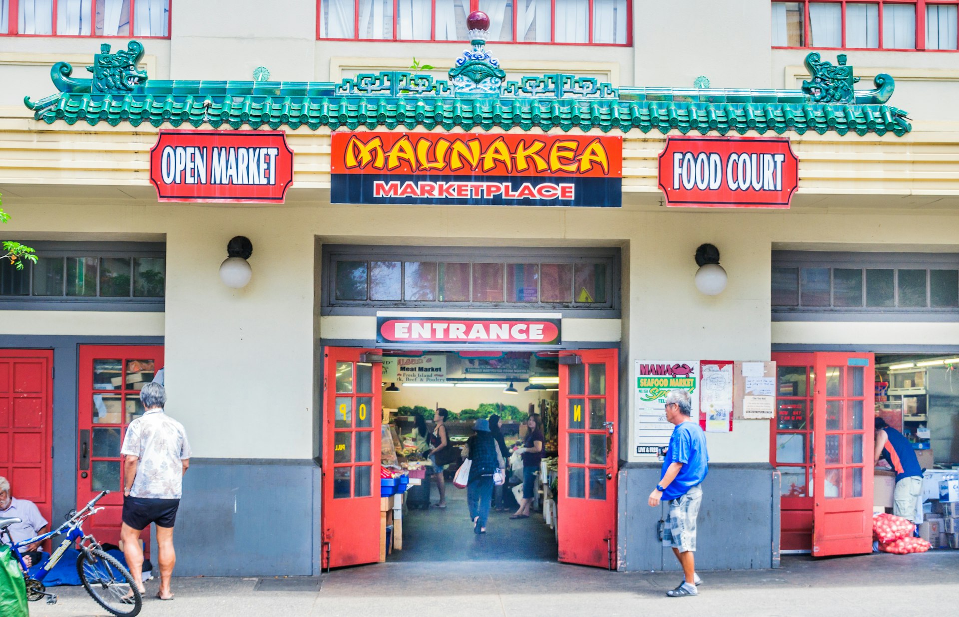 The exterior of a white building with red signs that read: "Open market", "Maunakea Marketplace" And "Food Bank"