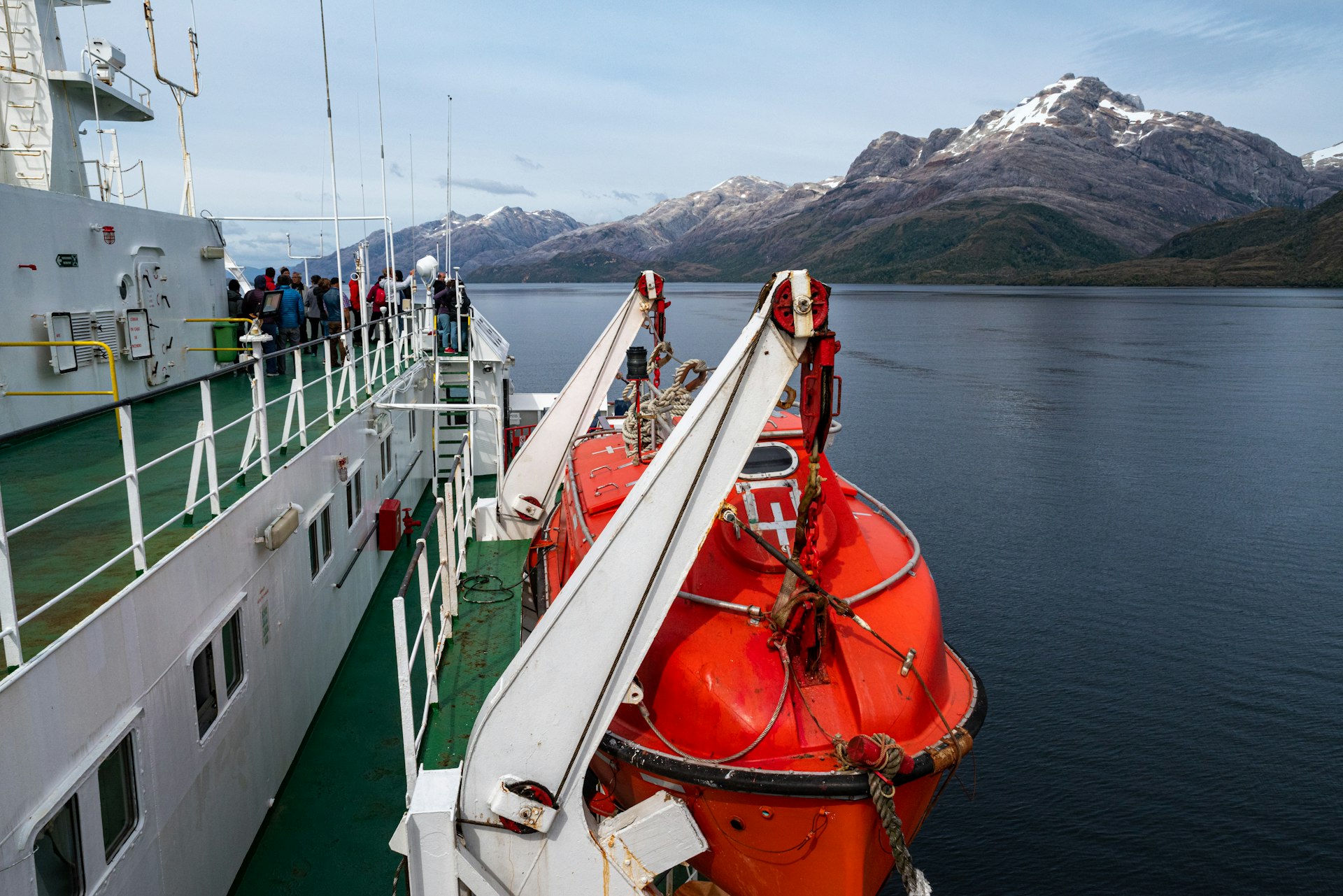 A cruise ship in fjords with passengers at the front enjoying the scenery