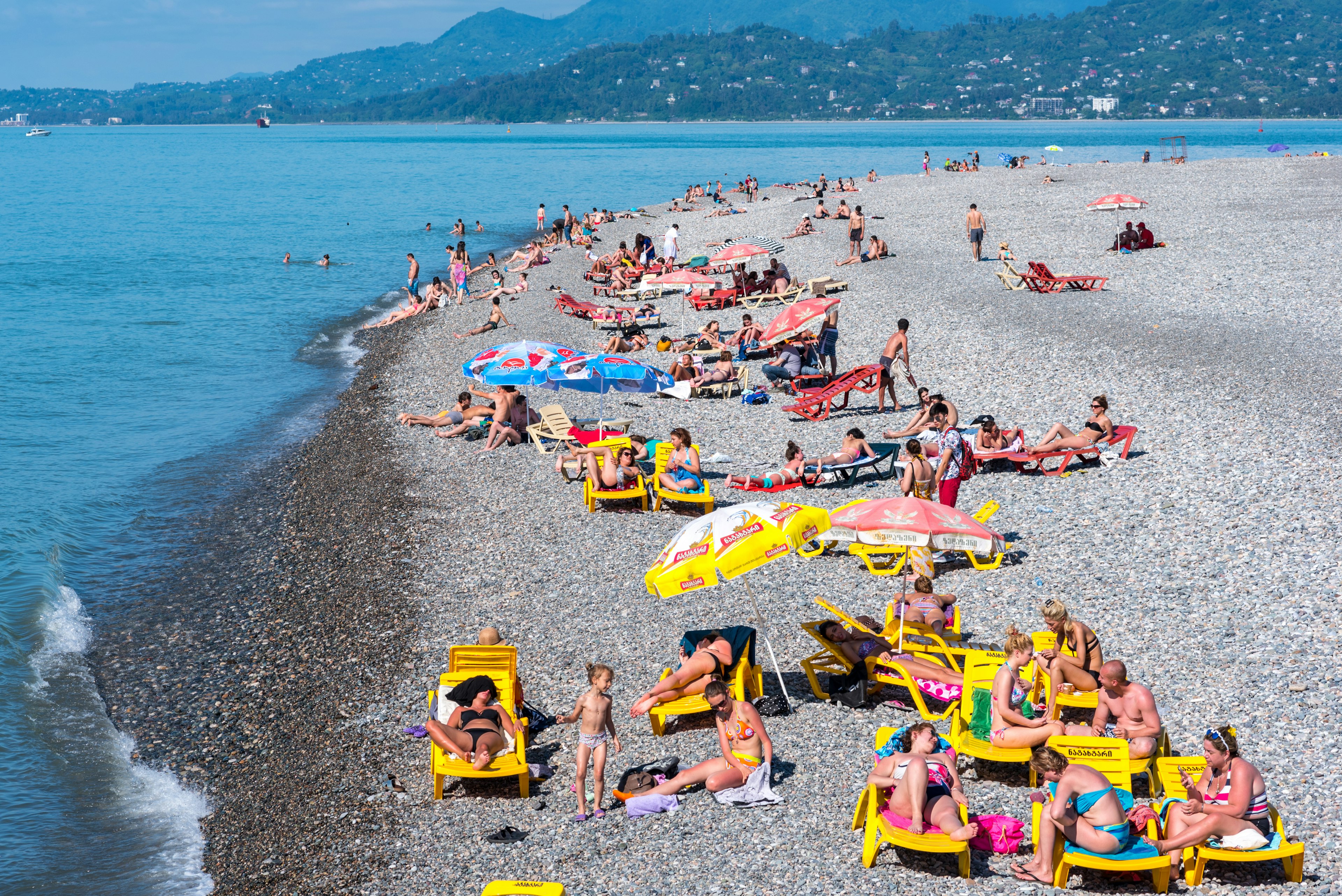 Crowds of people are relaxing on a pebble beach on a sunny day