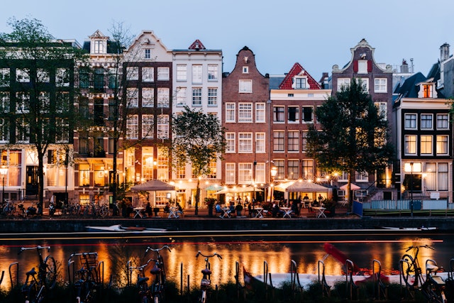 People sit at canalside tables outside bars and restaurants lit by string lights in the evening