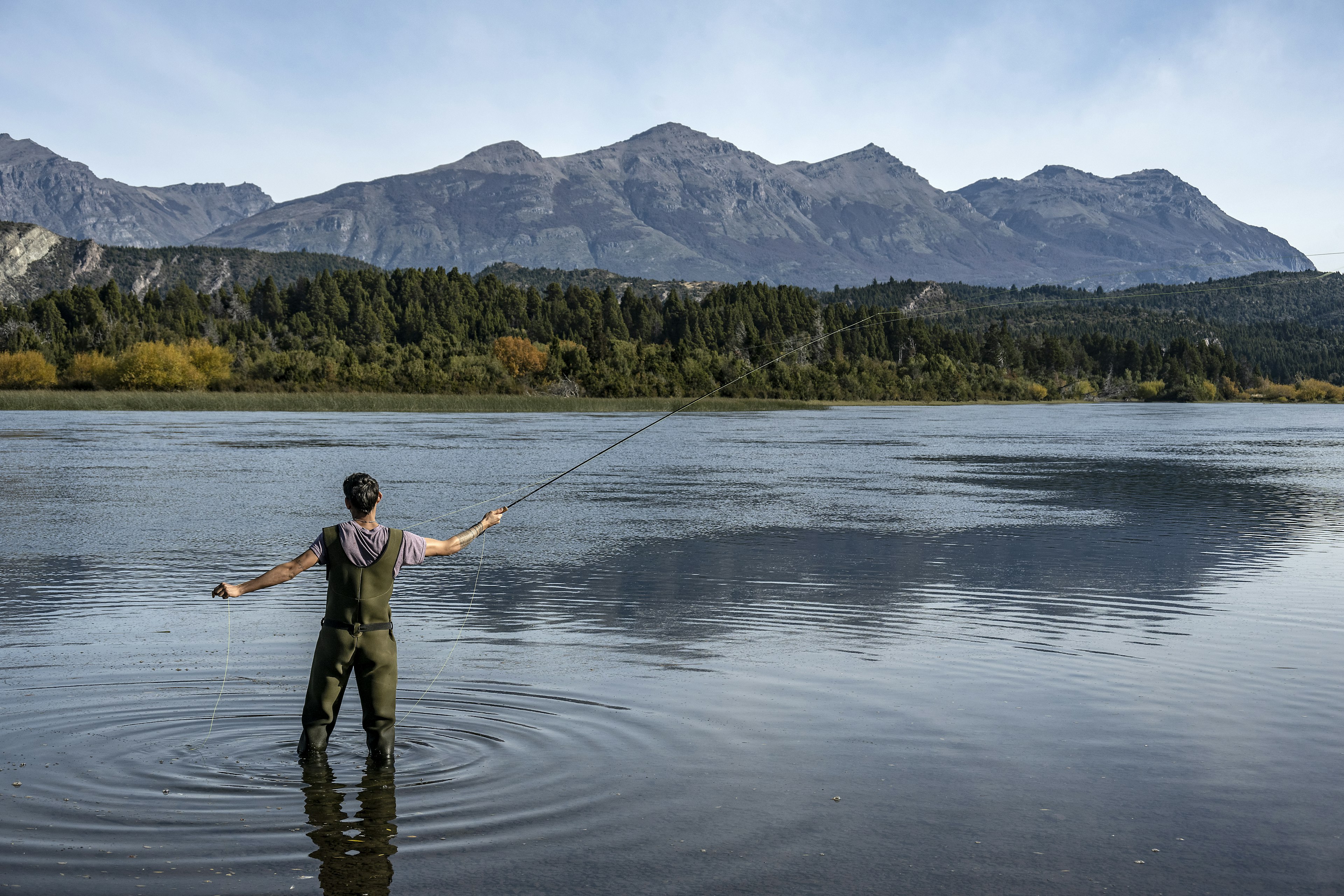 A man fly-fishing in a river in a hilly region