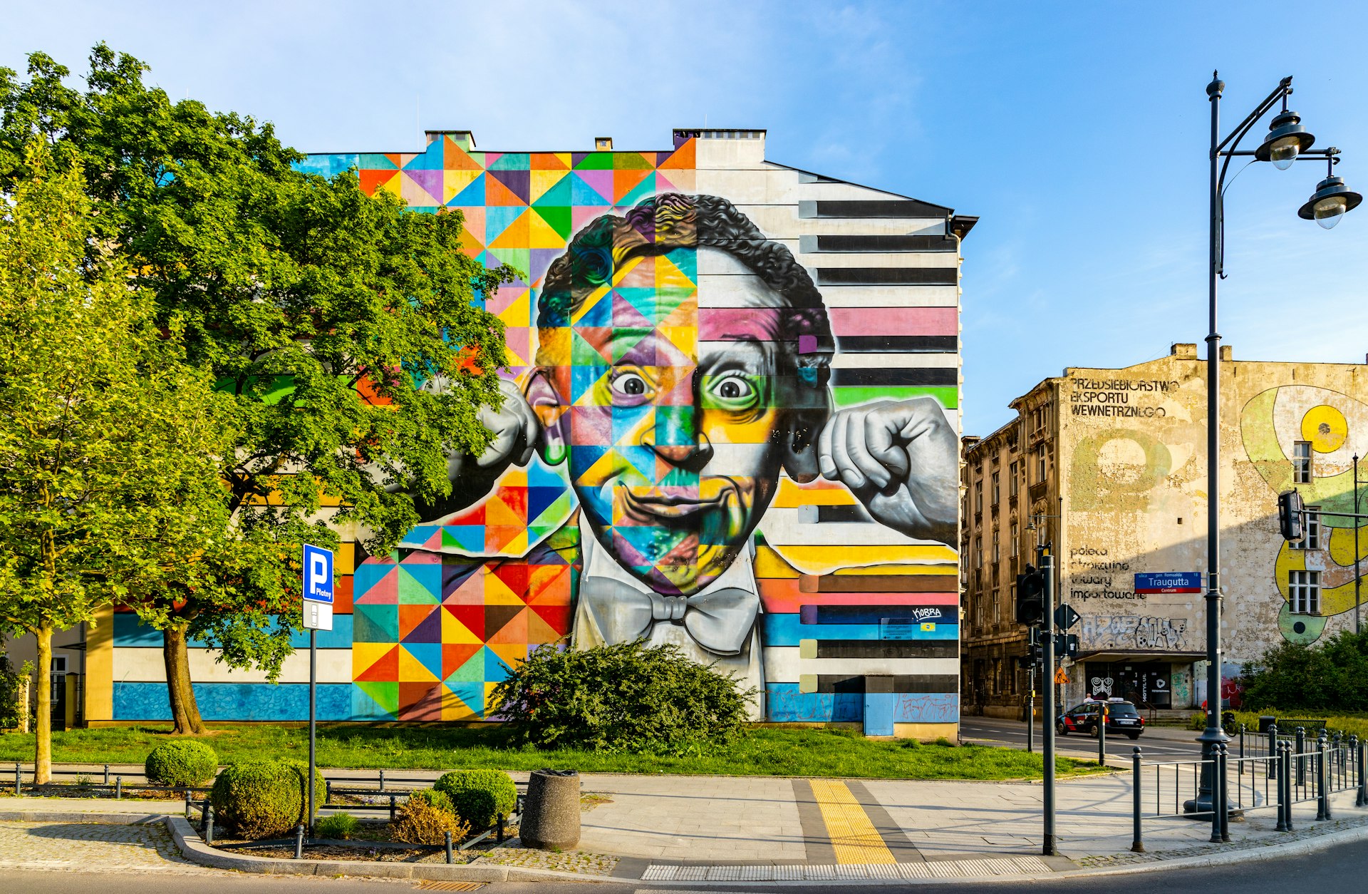 A colorful mural depicting a man pulling a funny face is painted on the side of a building in Łódź 