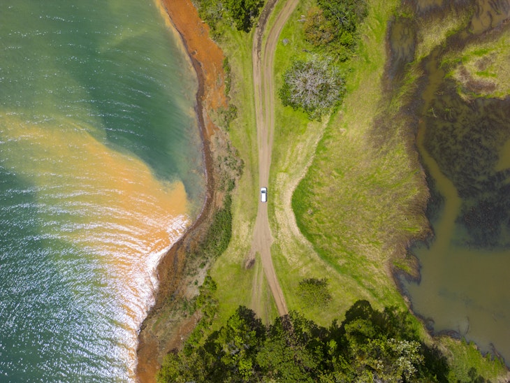 Dominical, Costa Rica - An aerial view of a car driving along a dirt road surrounded by water on either side.  © Jordan Siemens / Getty Images