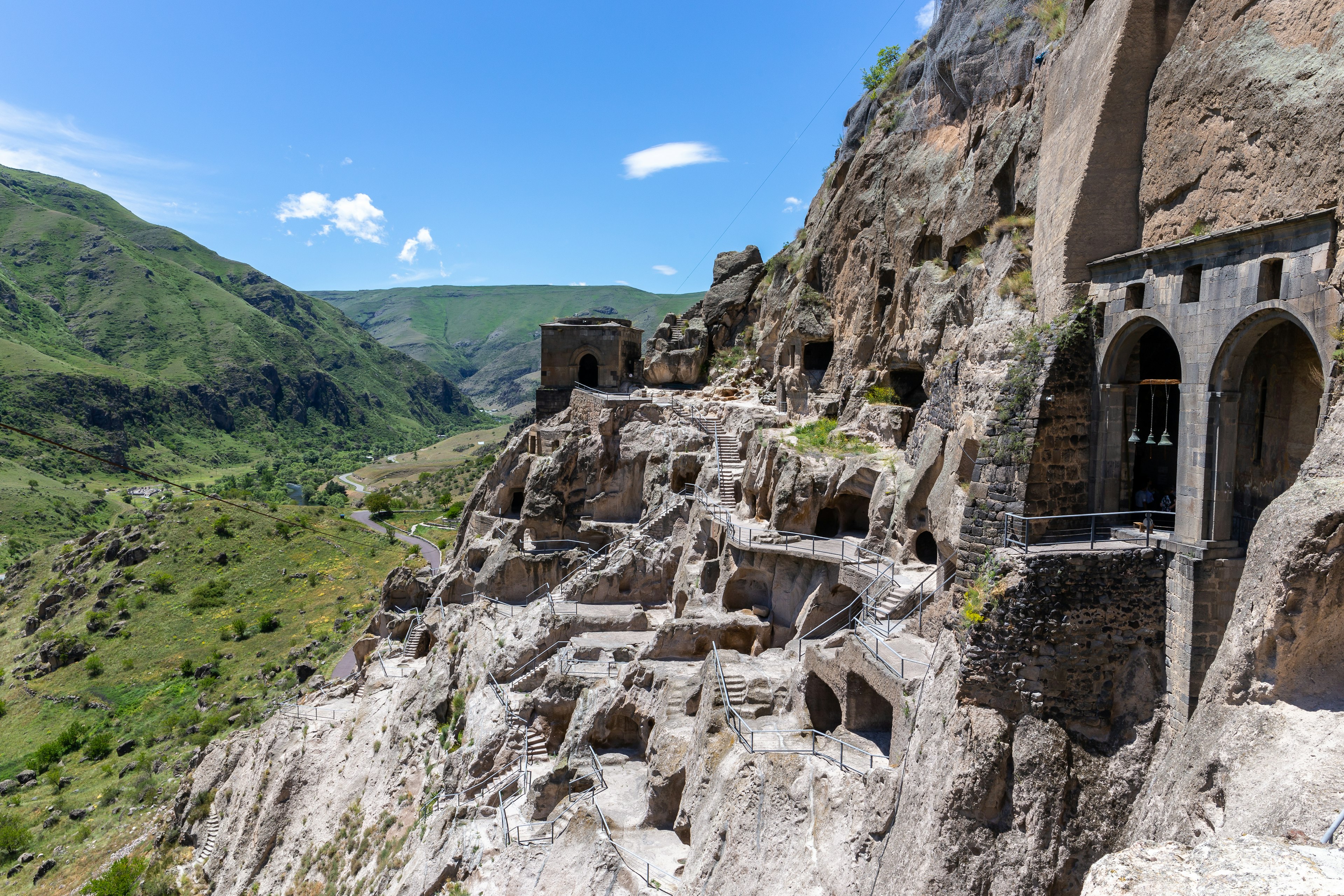 A mountain escarpment with caves, tunnels and dwellings carved into the rock. There's a river valley in the background.