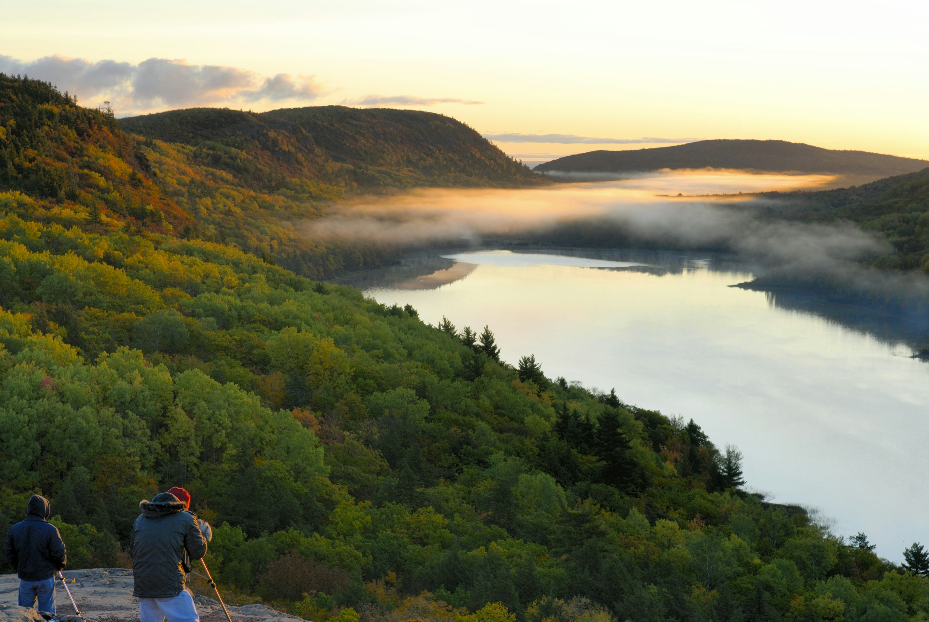 Two photographers take photos of an early morning cloud over a lake in woodland