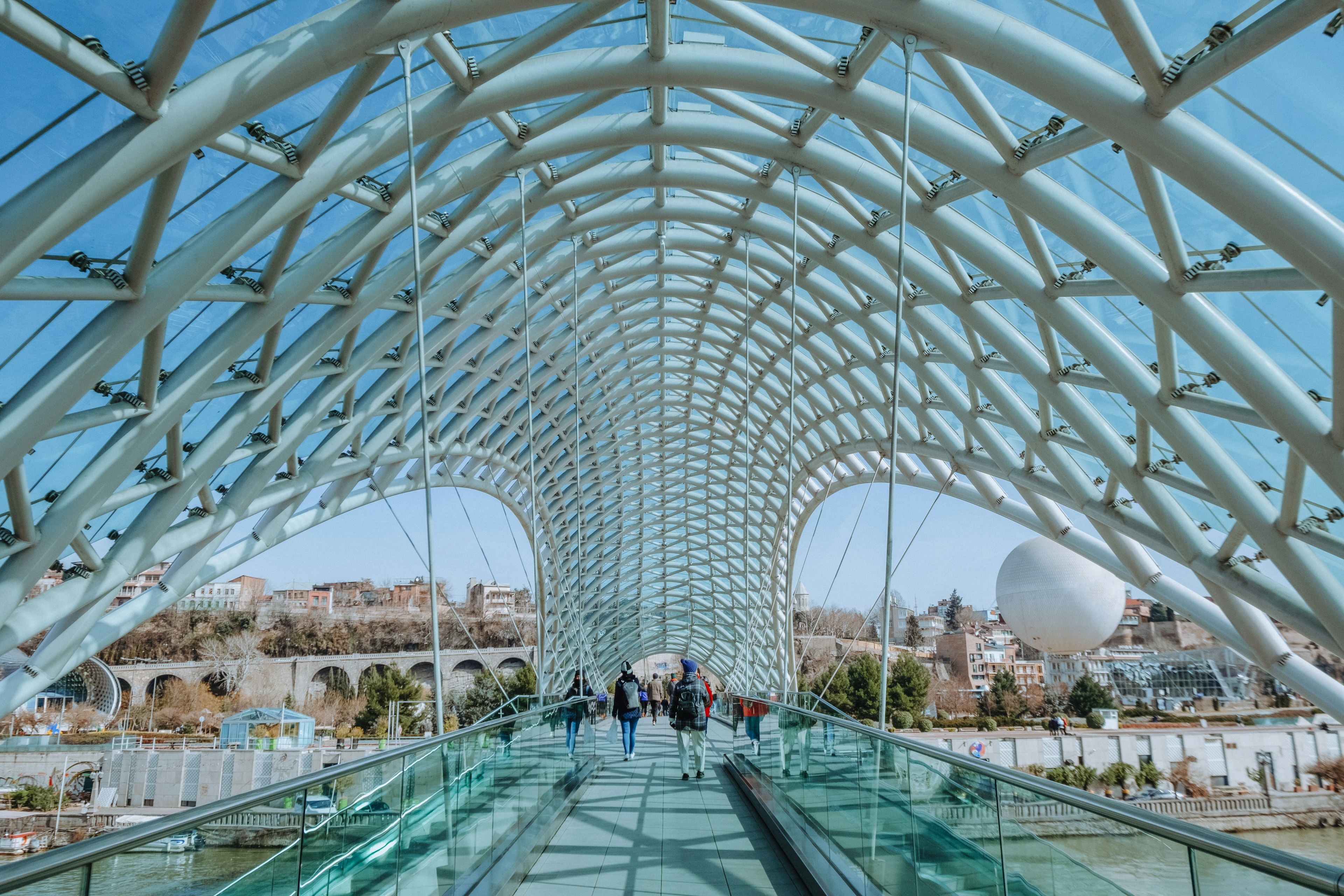 A bridge over a river. The architecture of the bridge has a network of grey metal and glass that stretches over the bulk of the bridge