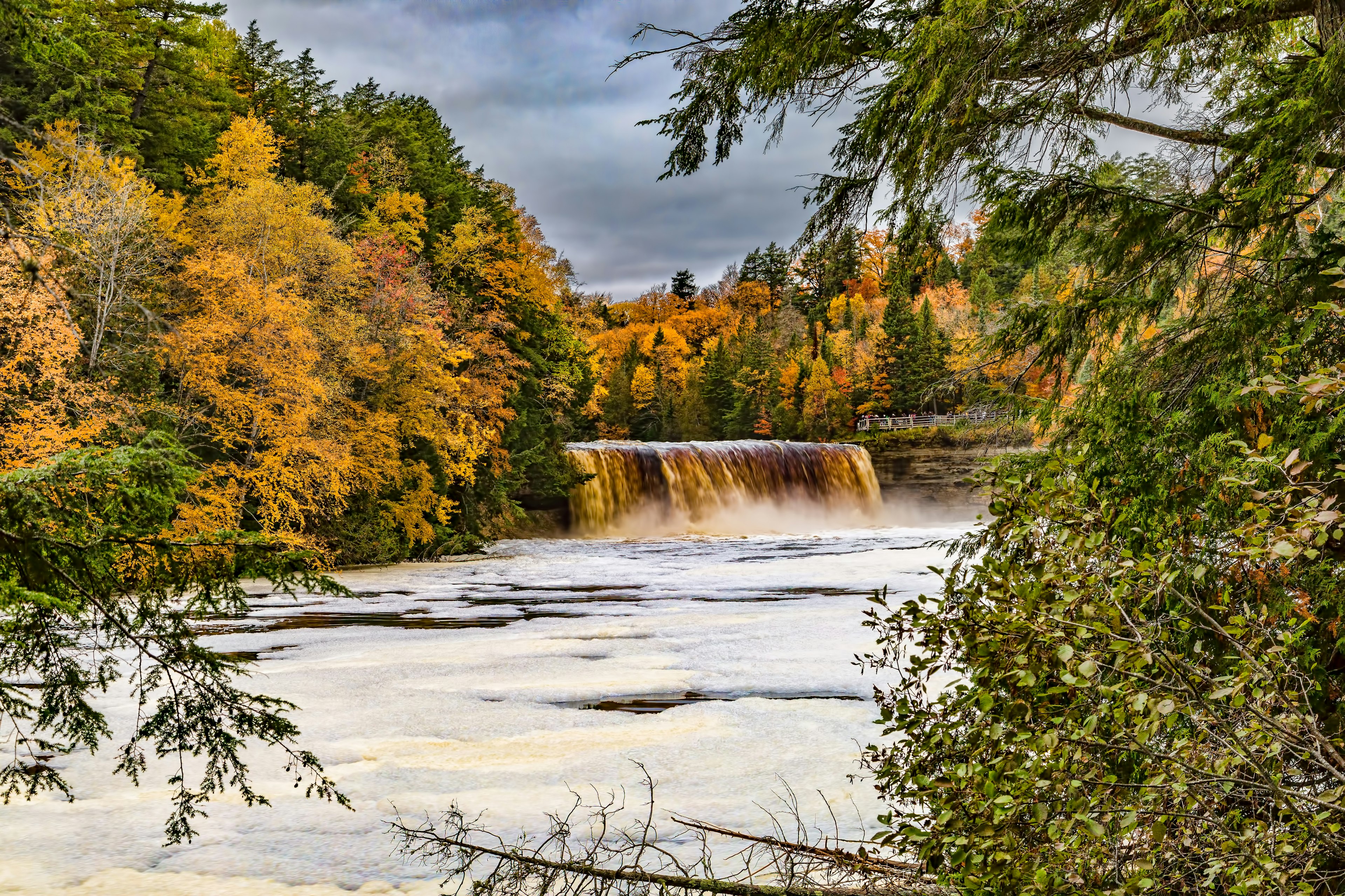 A waterfall cascading down into a pool in a river surrounded by woodland