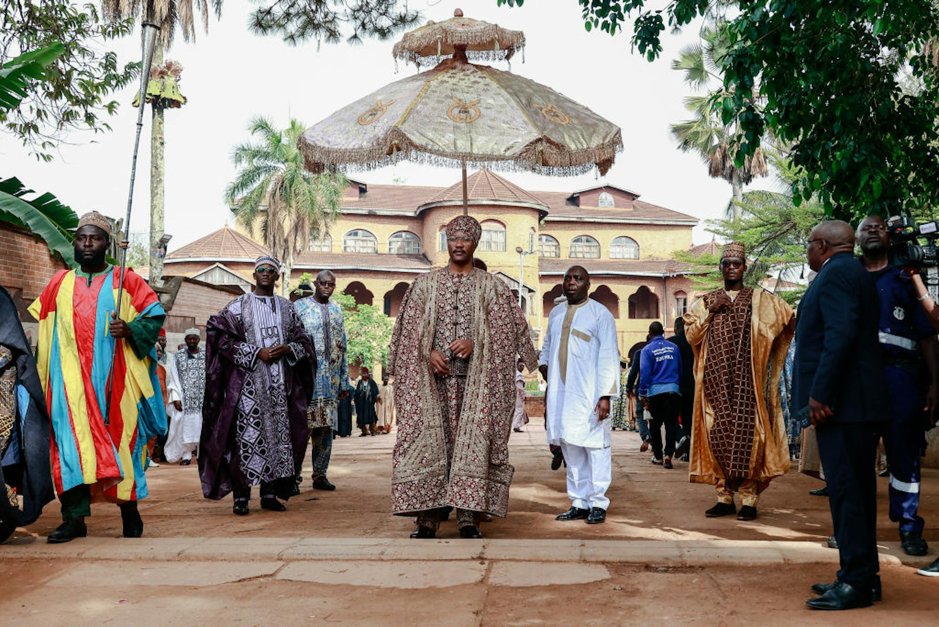 The Sultan King of the Bamouns walks in front of a palace at a ceremony with many men standing around