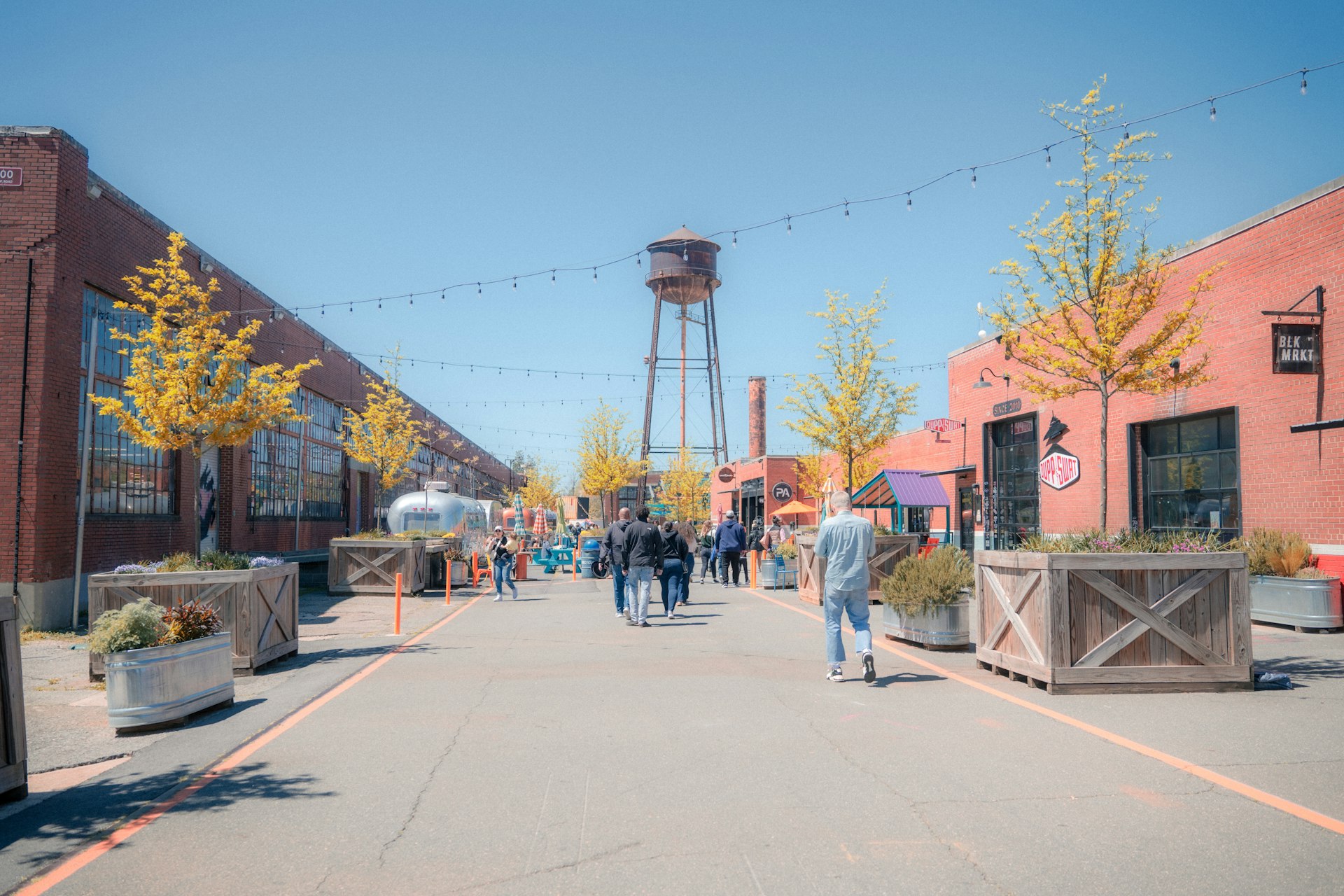 People walk through an outdoor retail space with a large water tower at one end