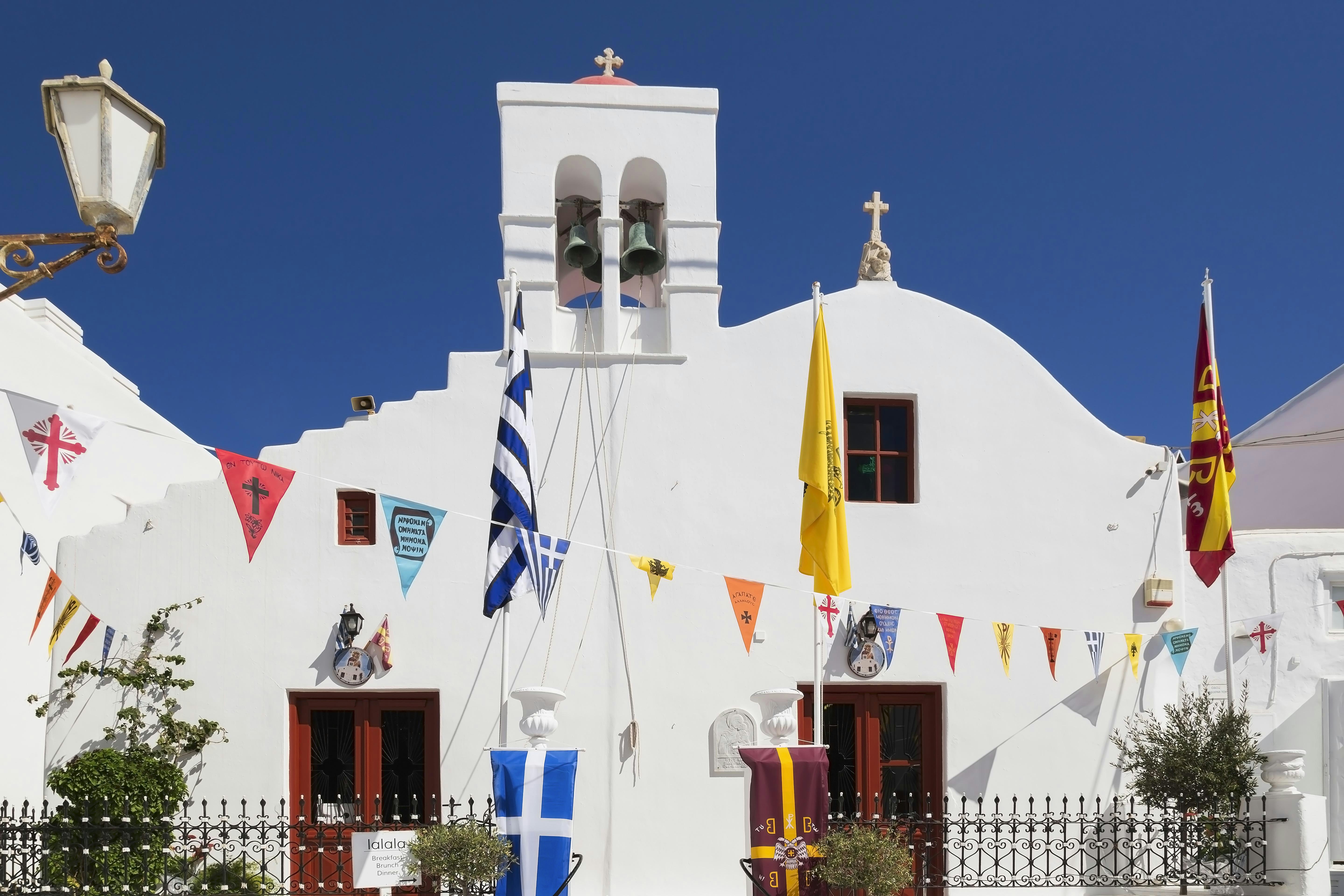 Greek Orthodox church and colourful flags hanging over narrow alley in Mykonos Town, Mykonos Island, Greece