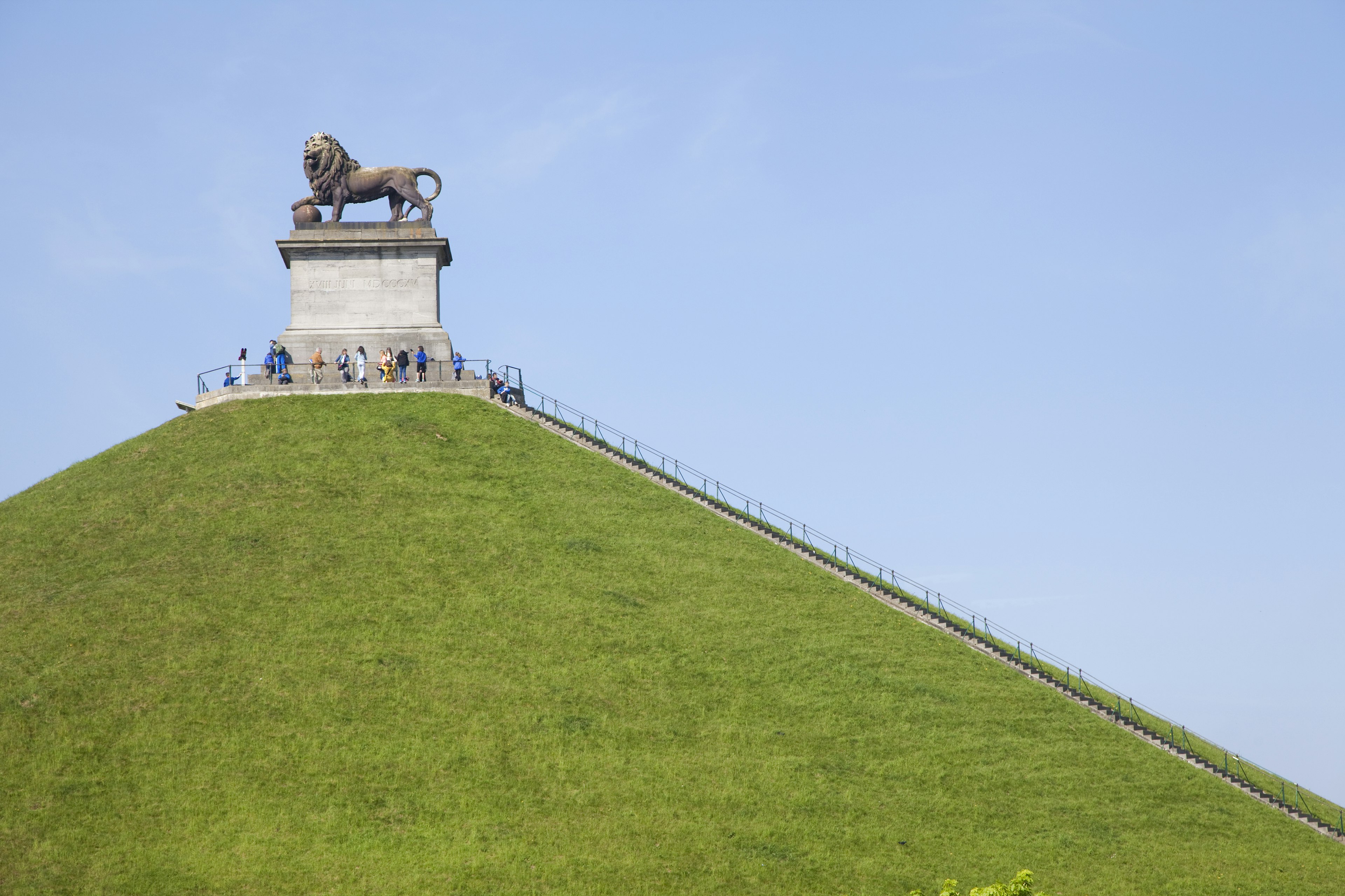 A grass-covered mound of earth with steps leading upwards to a large plinth with a huge bronze lion statue on it