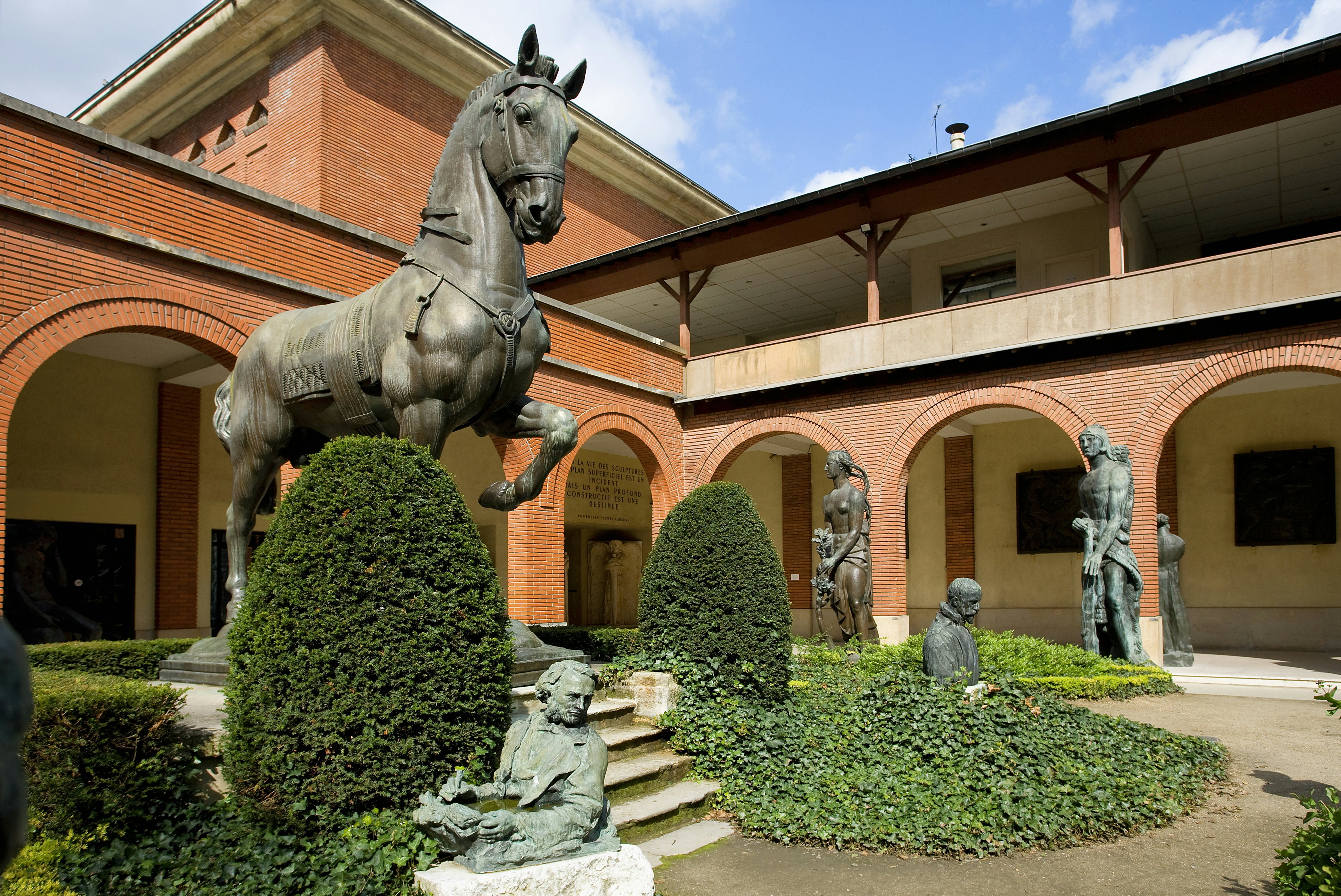 A large bronze scupture of a horse is displayed prominently in the garden of the Musée Bourdelle. Several other sculptures stand amid the topiary and manicured hedges.