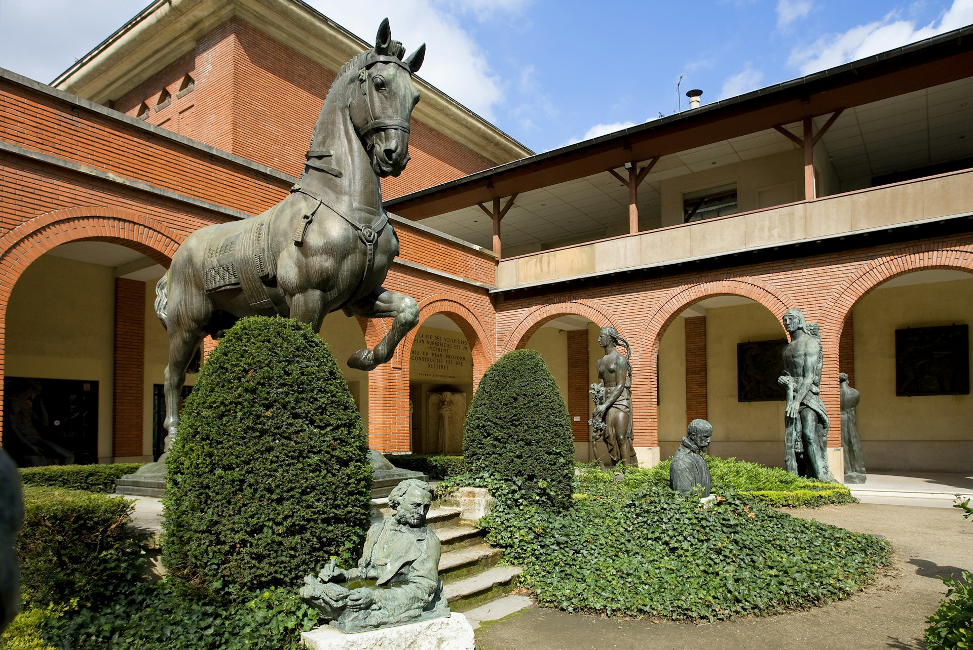 A large bronze scupture of a horse is displayed prominently in the garden of the Musée Bourdelle. Several other sculptures stand amid the topiary and manicured hedges.
