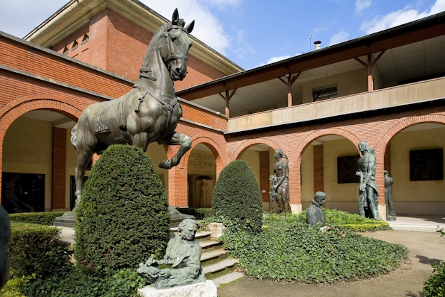 A large bronze scupture of a horse is displayed prominently in the garden of the Musée Bourdelle. Several other sculptures stand amid the topiary and manicured hedges.