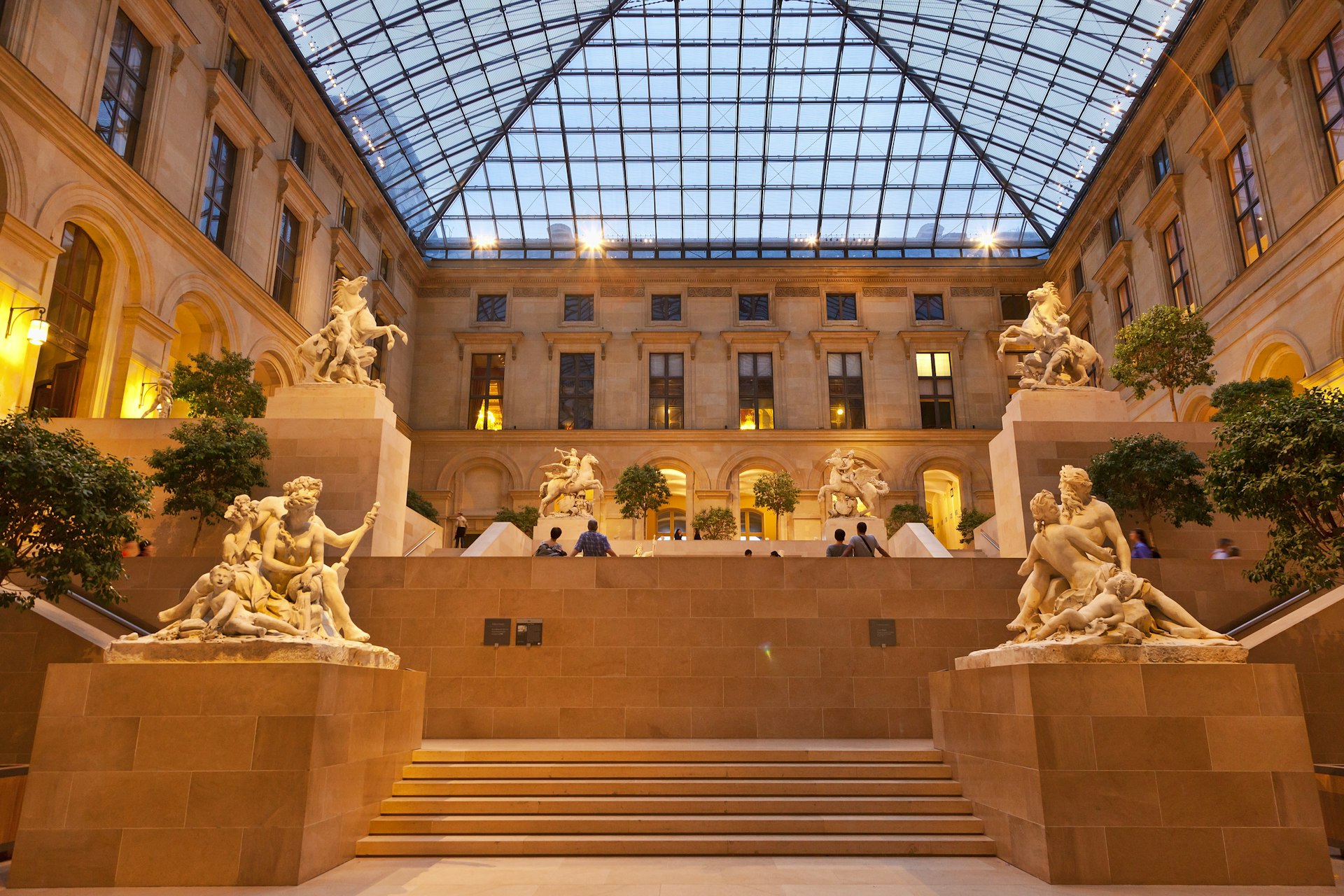 People are admiring the sculptures in the Cour Marly, a vast atrium with a huge glass ceiling inside the Louvre in Paris.