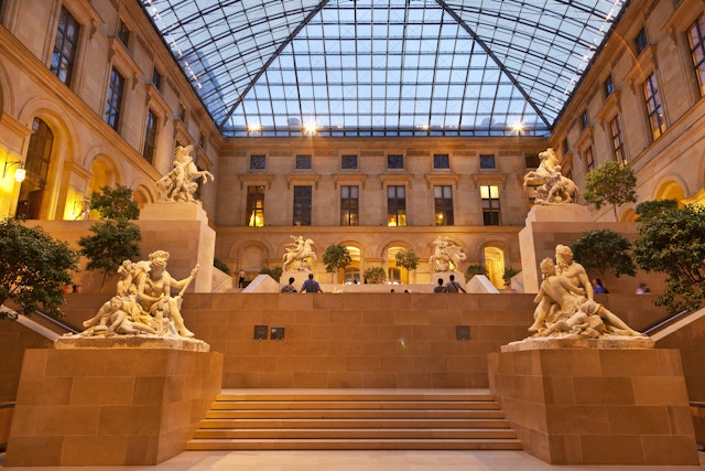 People are admiring the sculptures in the Cour Marly, a vast atrium with a huge glass ceiling inside the Louvre in Paris.