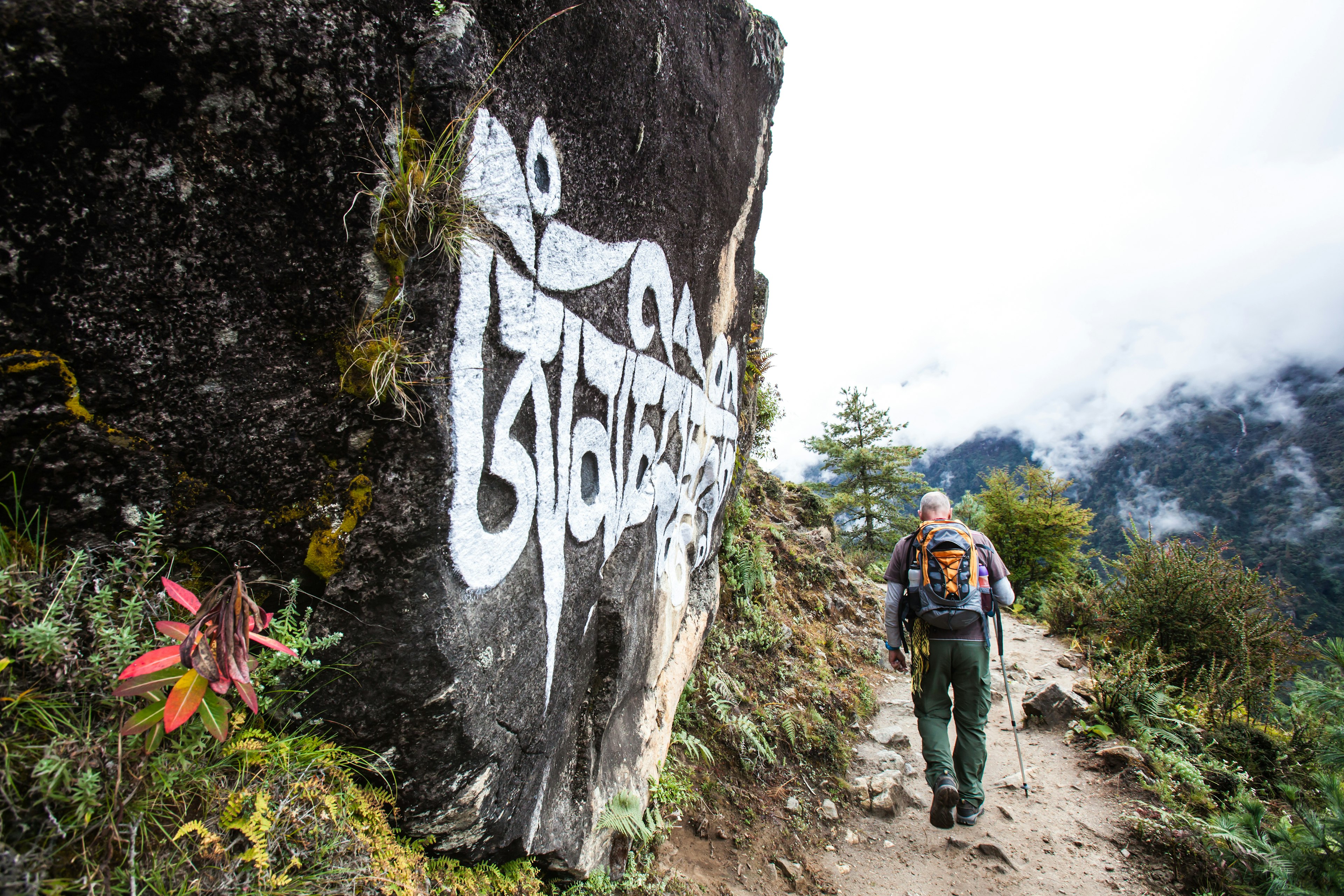 A solo trekker follows a path through a mountainous area where clouds hang low over the hills